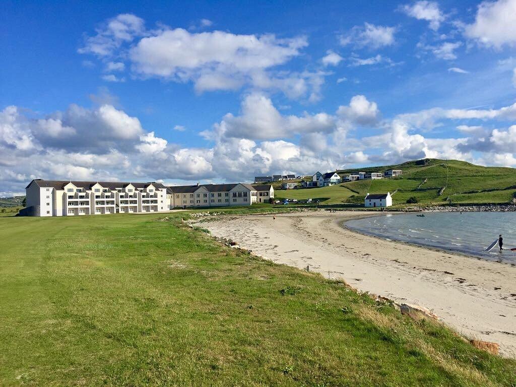 Overview of the resort building just next to the beach with a gentleman standing in the water with his surfboard