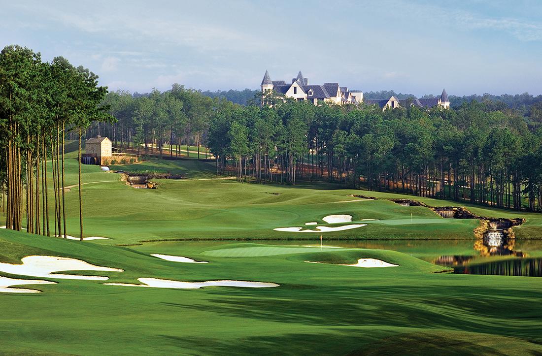 Uniquely shaped sand bunkers on the fairway leading to a smooth green with the resort building in the distance