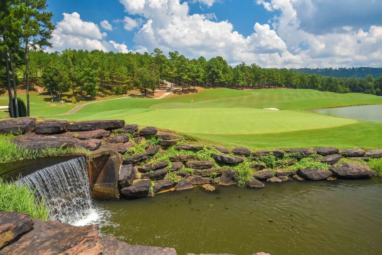 A rock themed water fountain flowing into a large water hazard on the Ross Bridge course next to a smooth green