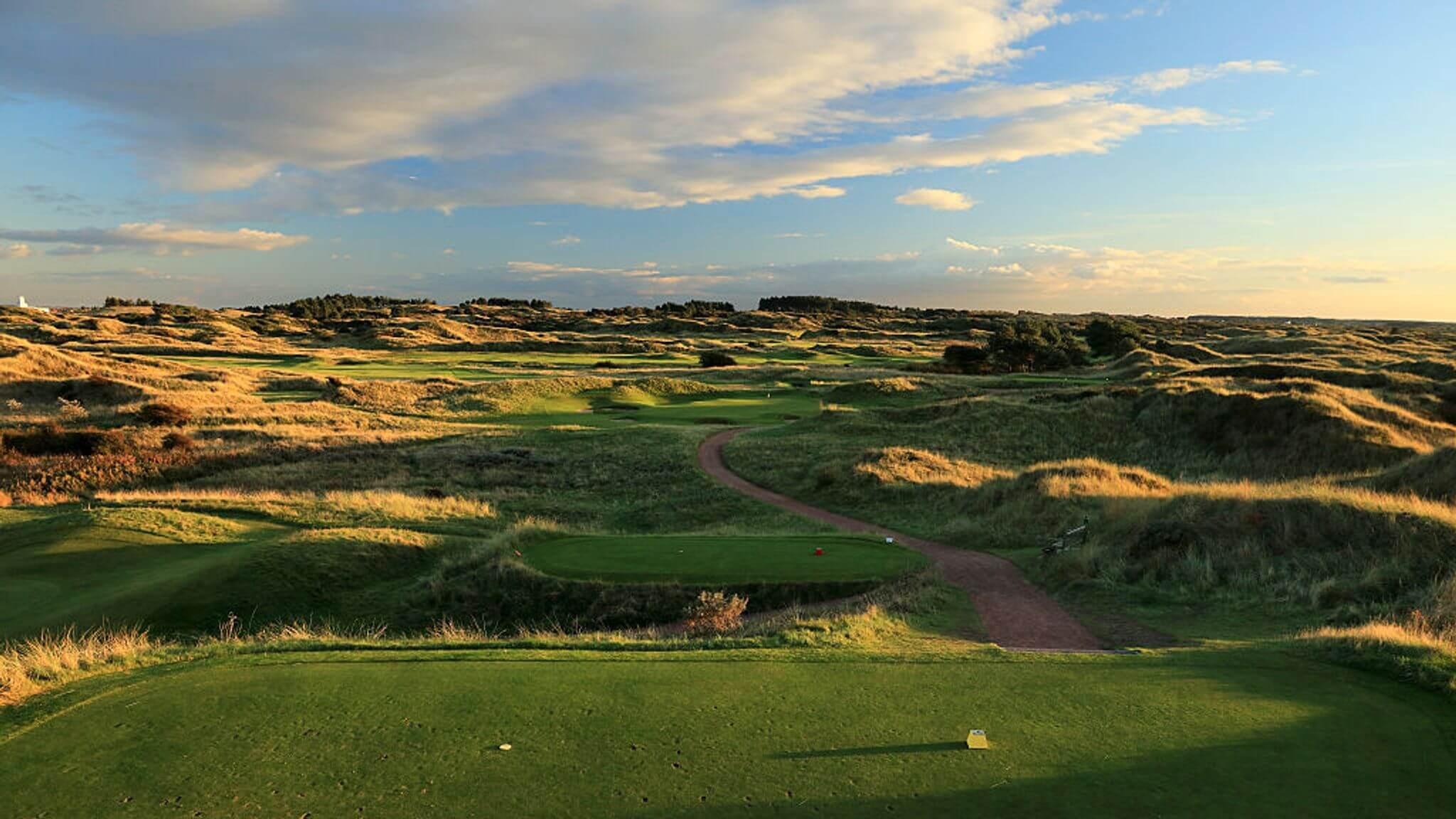 A serene golf course view with a winding path through golden dunes at sunset.