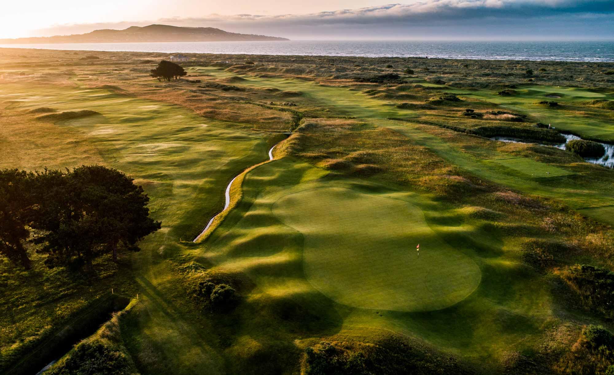 A stunning golf course at sunset, with rolling greens and the ocean in the distance.