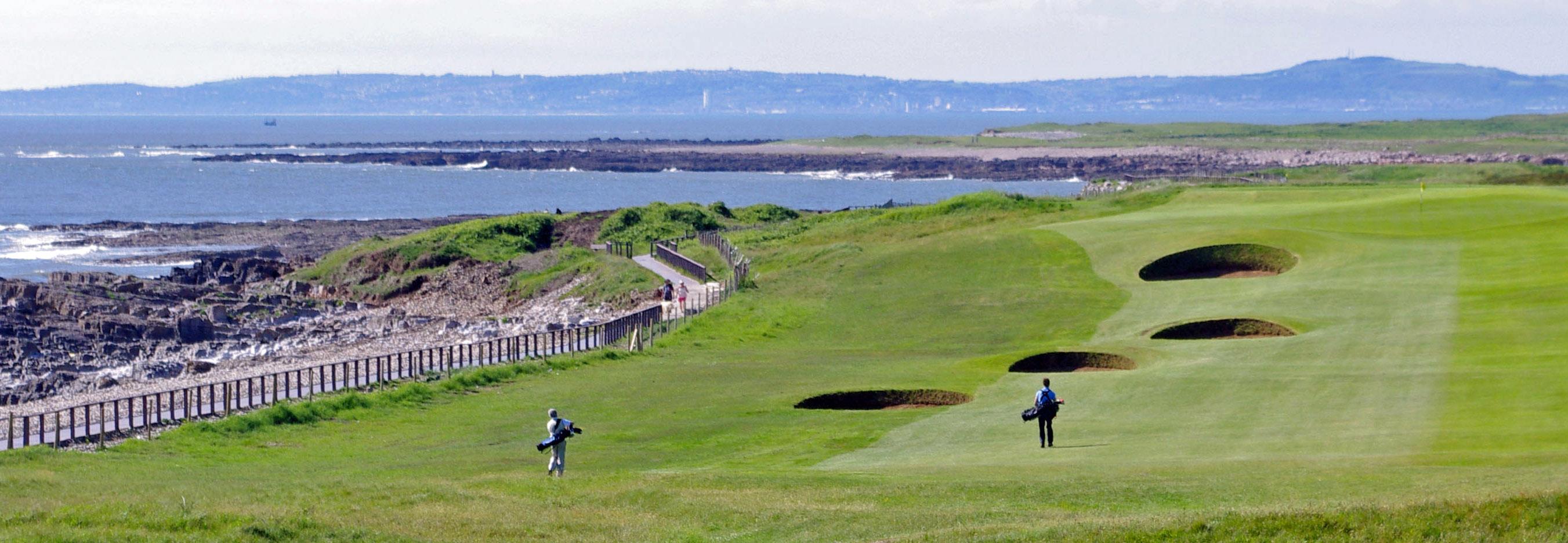 Golfers walking the Royal Porthcawl course with deep bunkers and a sea view