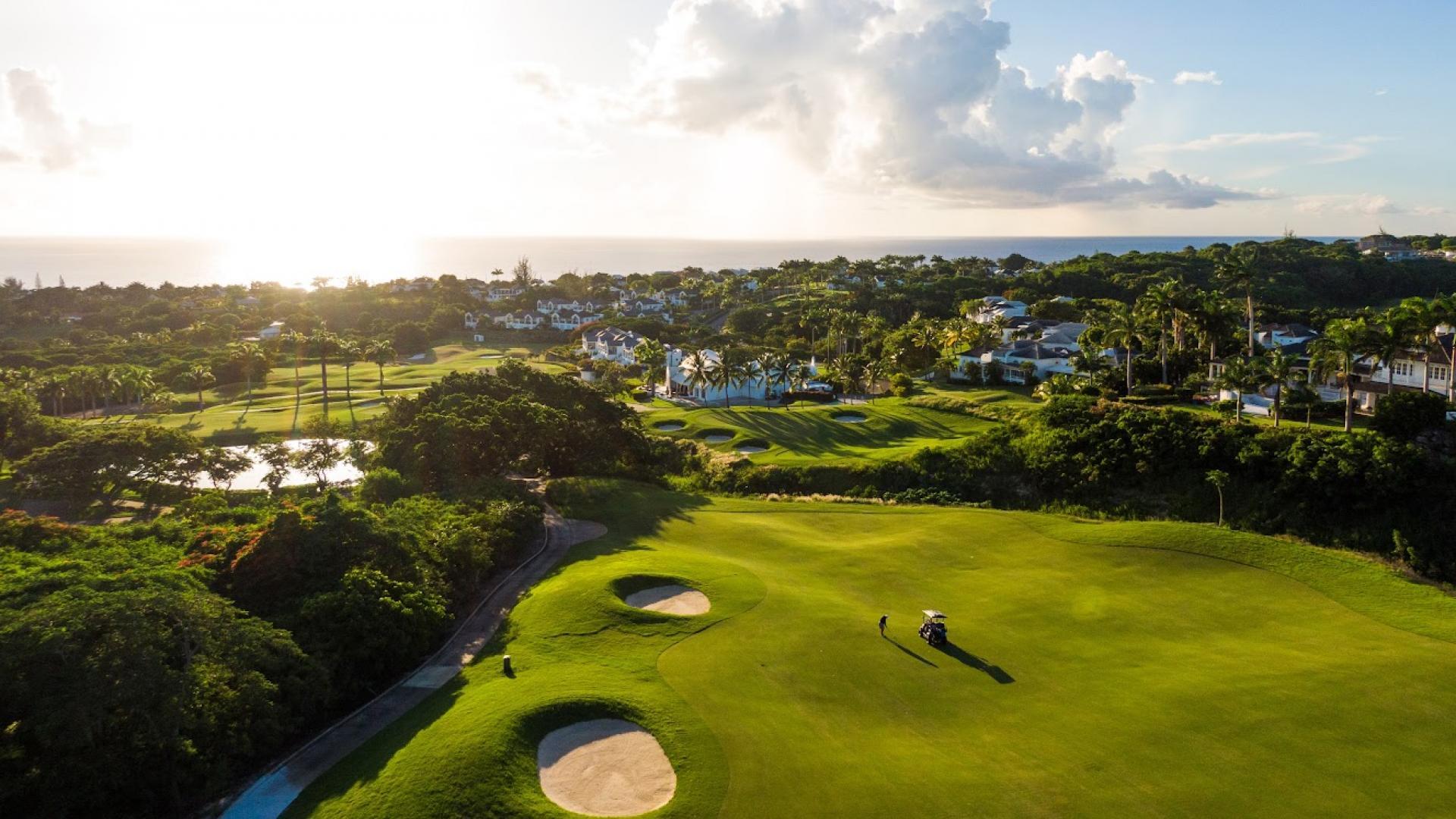 A beautiful sunset illuminates a coastal golf course with rolling greens and sand traps.