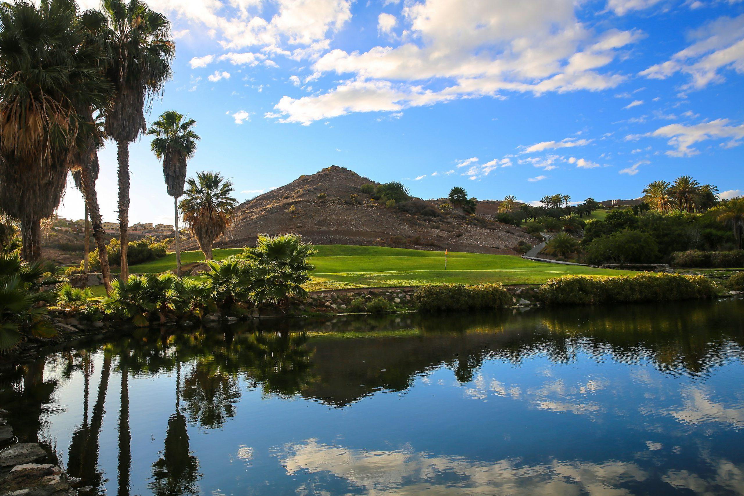 Water hazard in front of a green with hills behind it