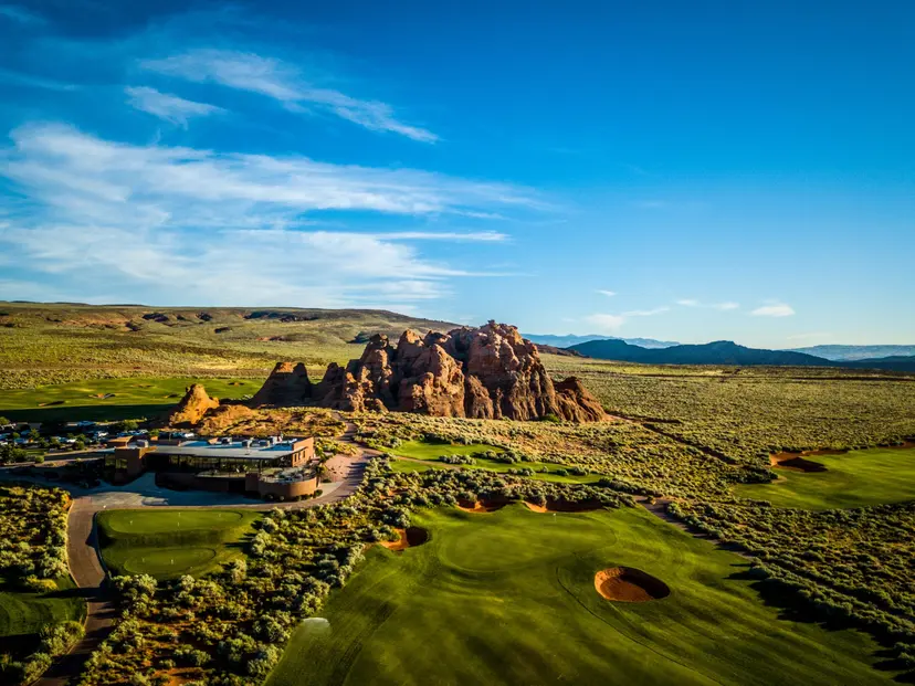 A clubhouse surrounded by vivid green fairways and striking red rock formations.