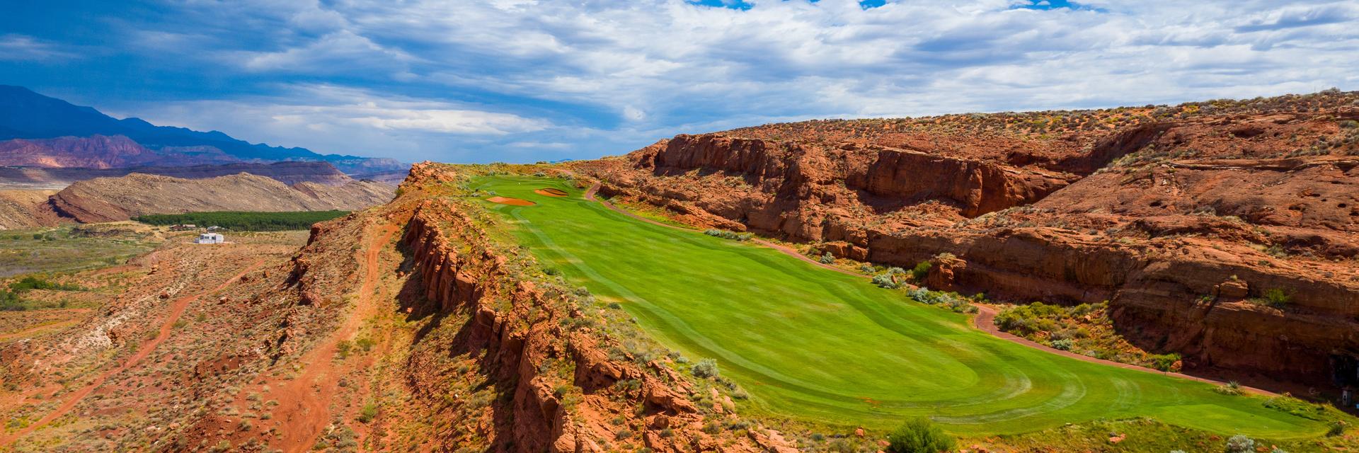 A narrow green fairway winds through dramatic red rock cliffs.