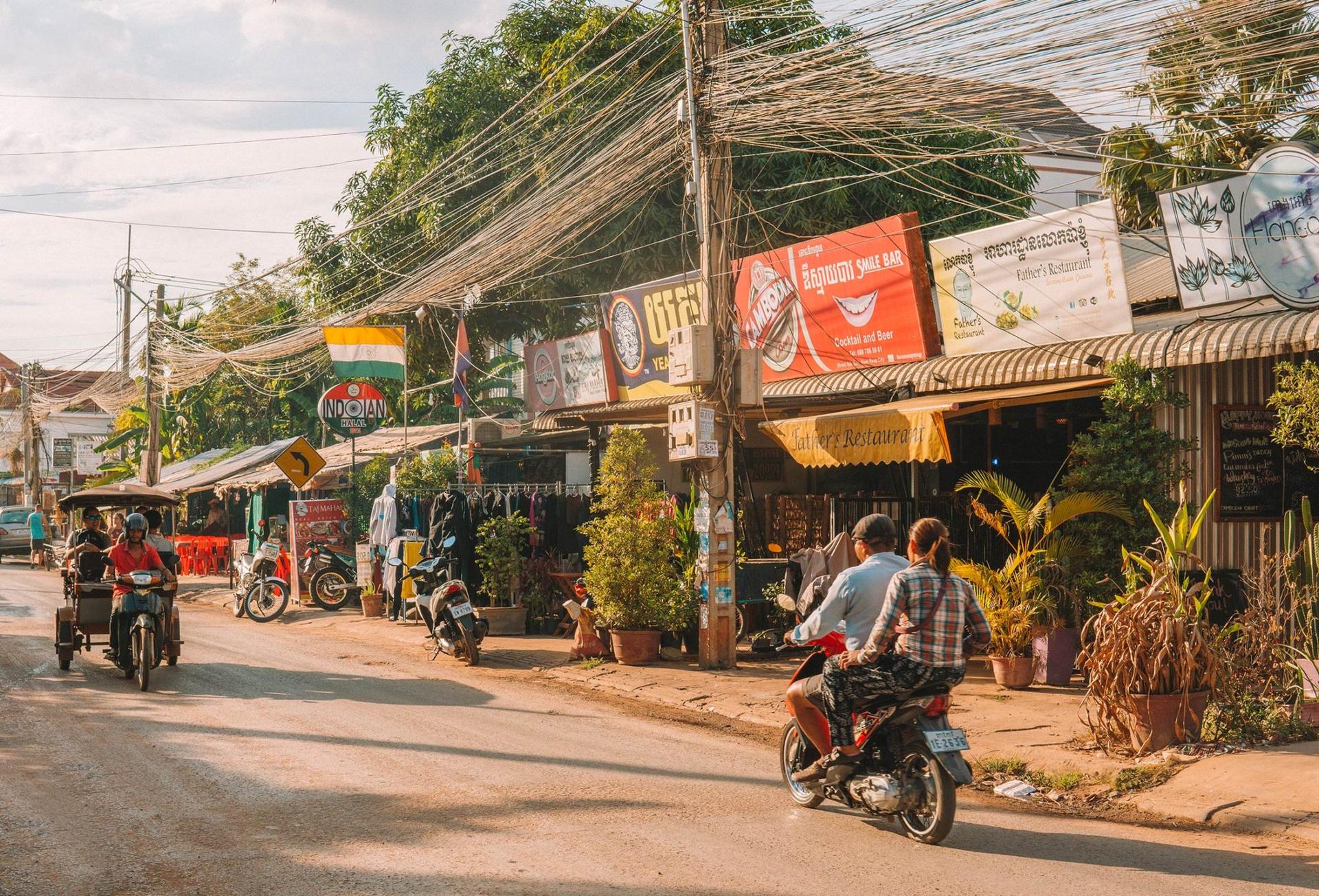 Two people on a motorbike and two more people on the back of a tuktuk taxi in Siem Reap