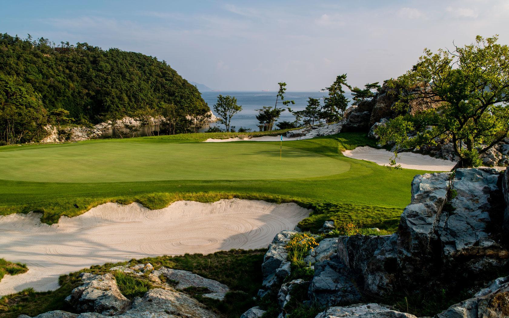 A smooth green surrounded by sand bunkers with coastal views