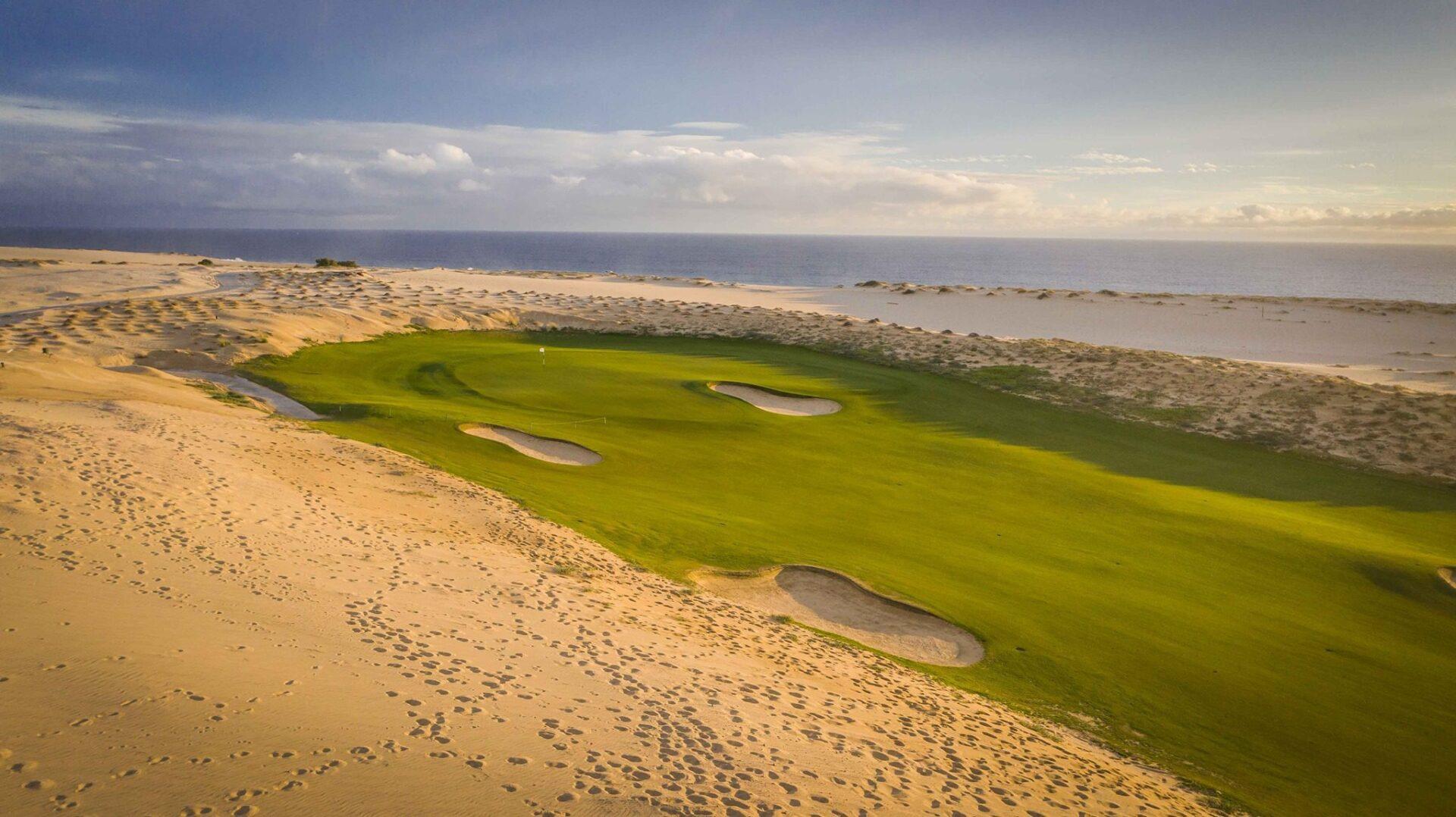 Elevated view of a wide fairway leading to a smooth green nestled with bunkers surrounded by a sandy rough