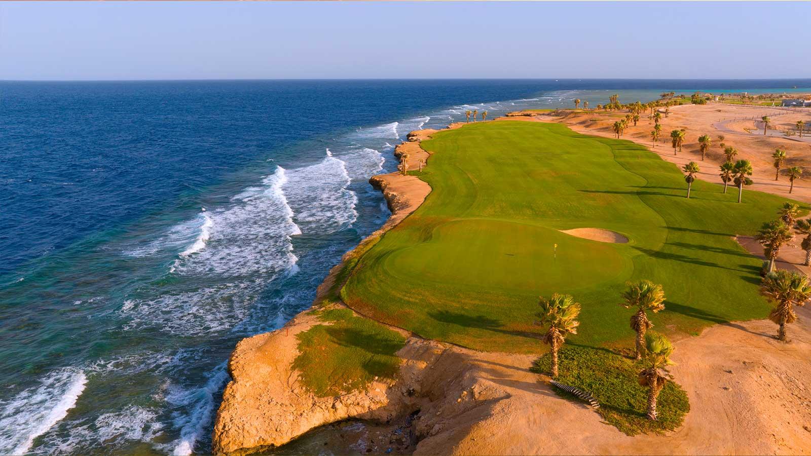 Aerial view of a smooth green on the Somabay Golf course with waves crashing in