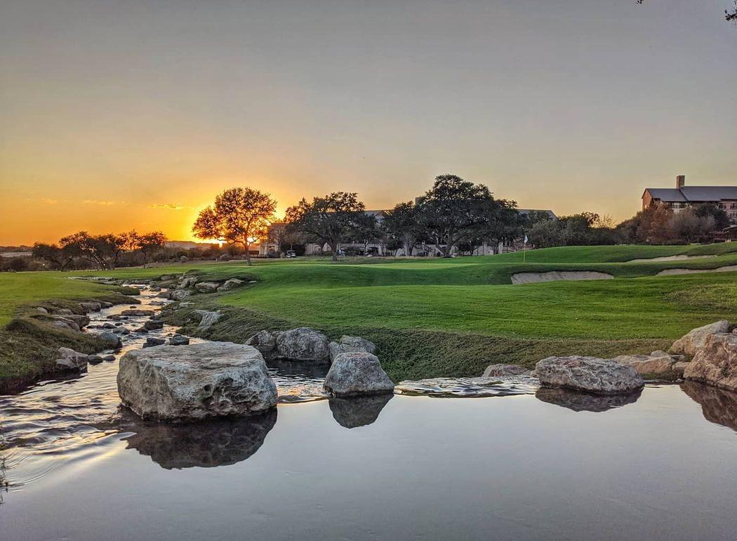 Tranquil stream flowing through the golf course with a vibrant sunset backdrop.