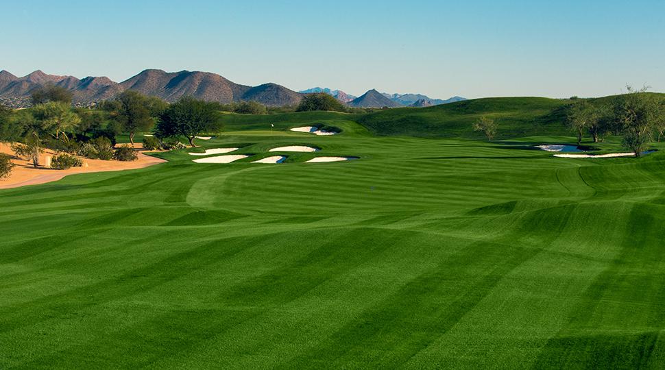 Rolling fairway lined with bunkers, with rugged desert mountains in the distance.