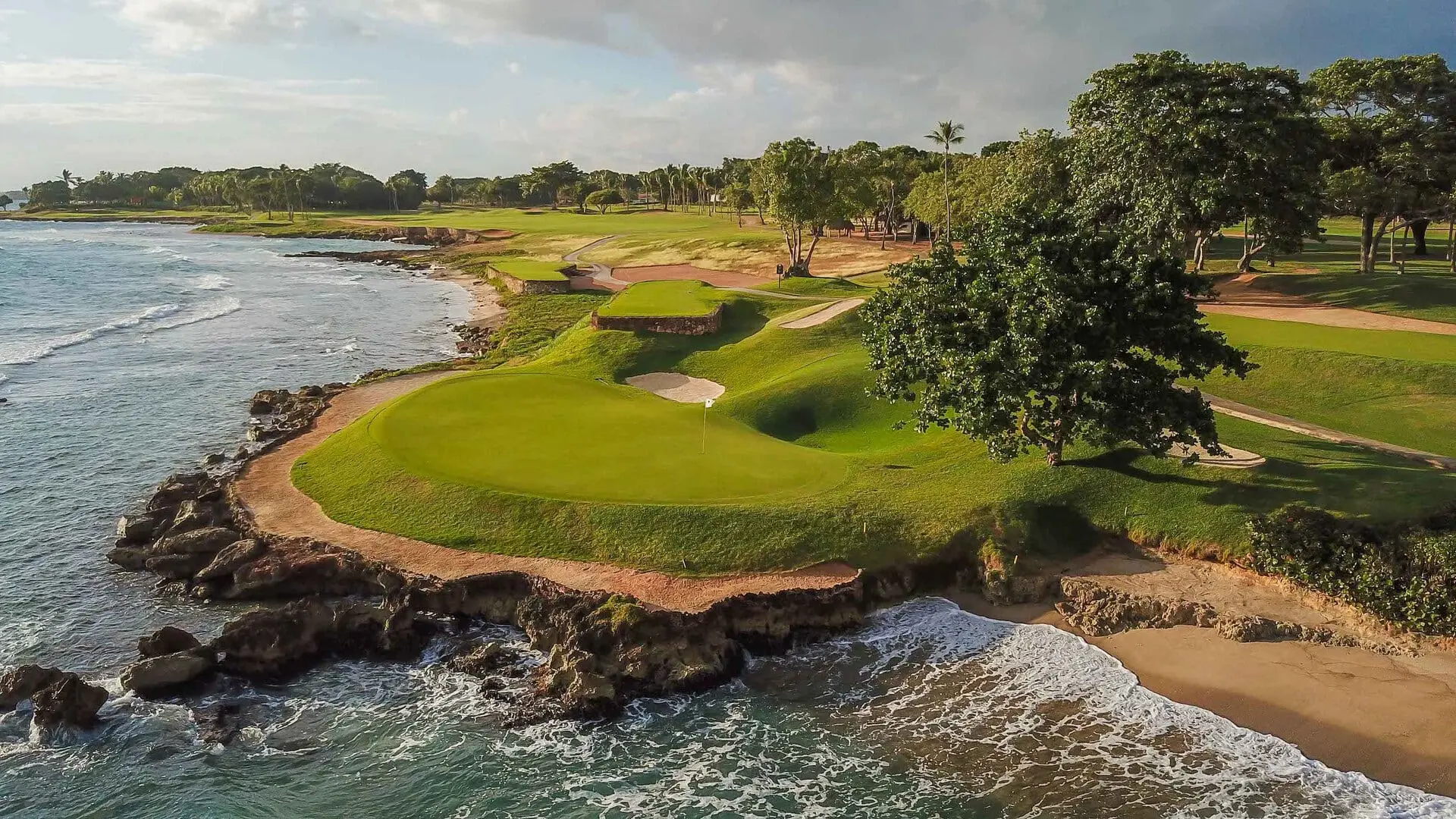 An elevated green surrounded by a large sand bunker next to the coast