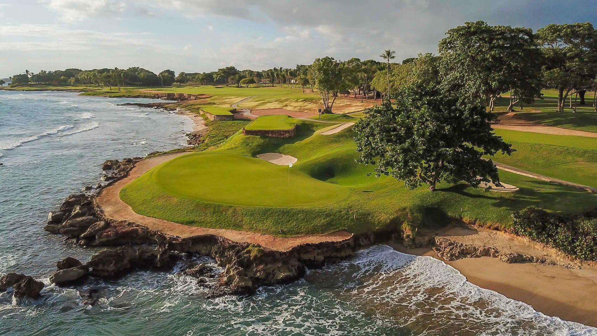 An elevated green surrounded by a large sand bunker next to the coast