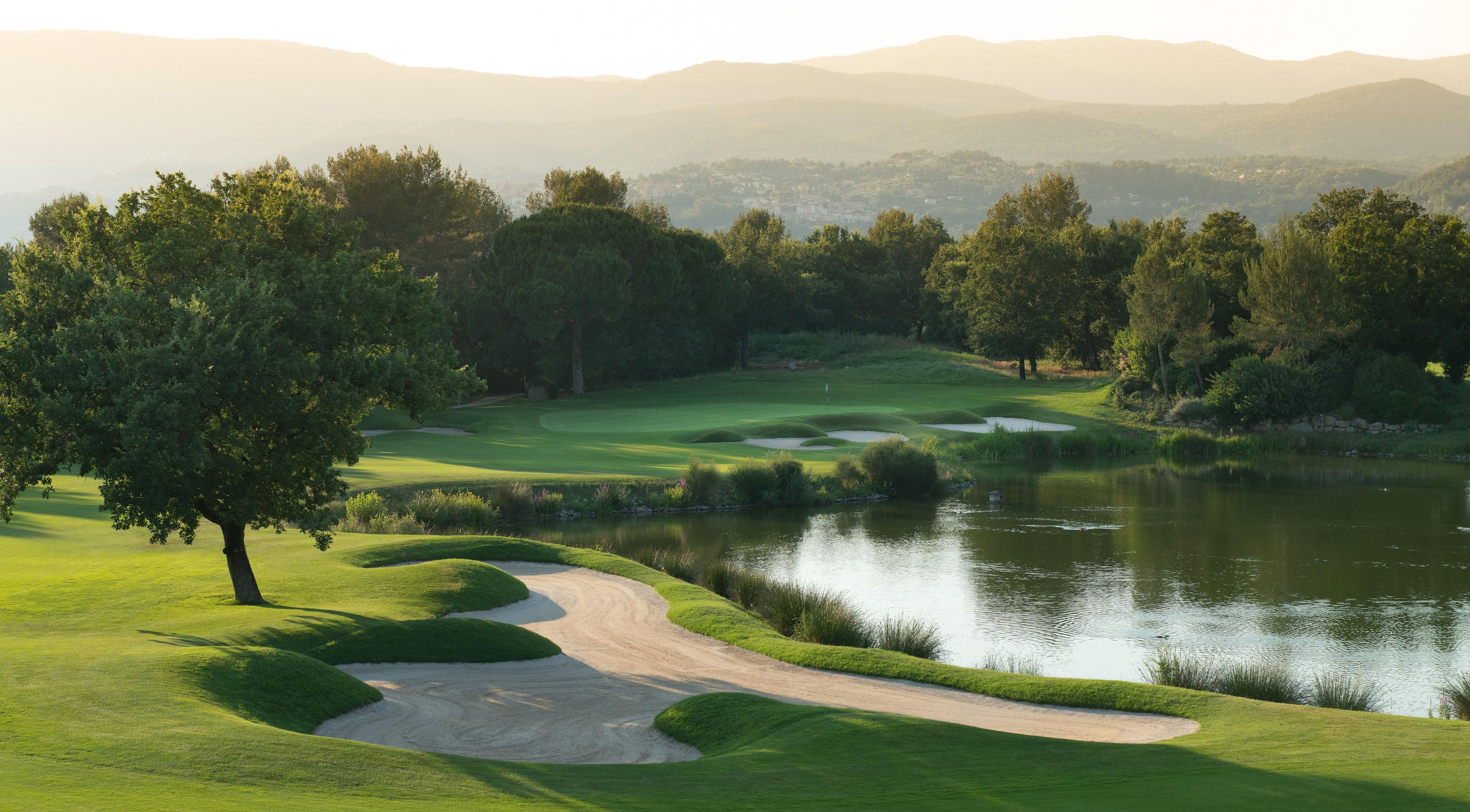 Narrow fairway with a water hazard on the right and views of the mountains in the background