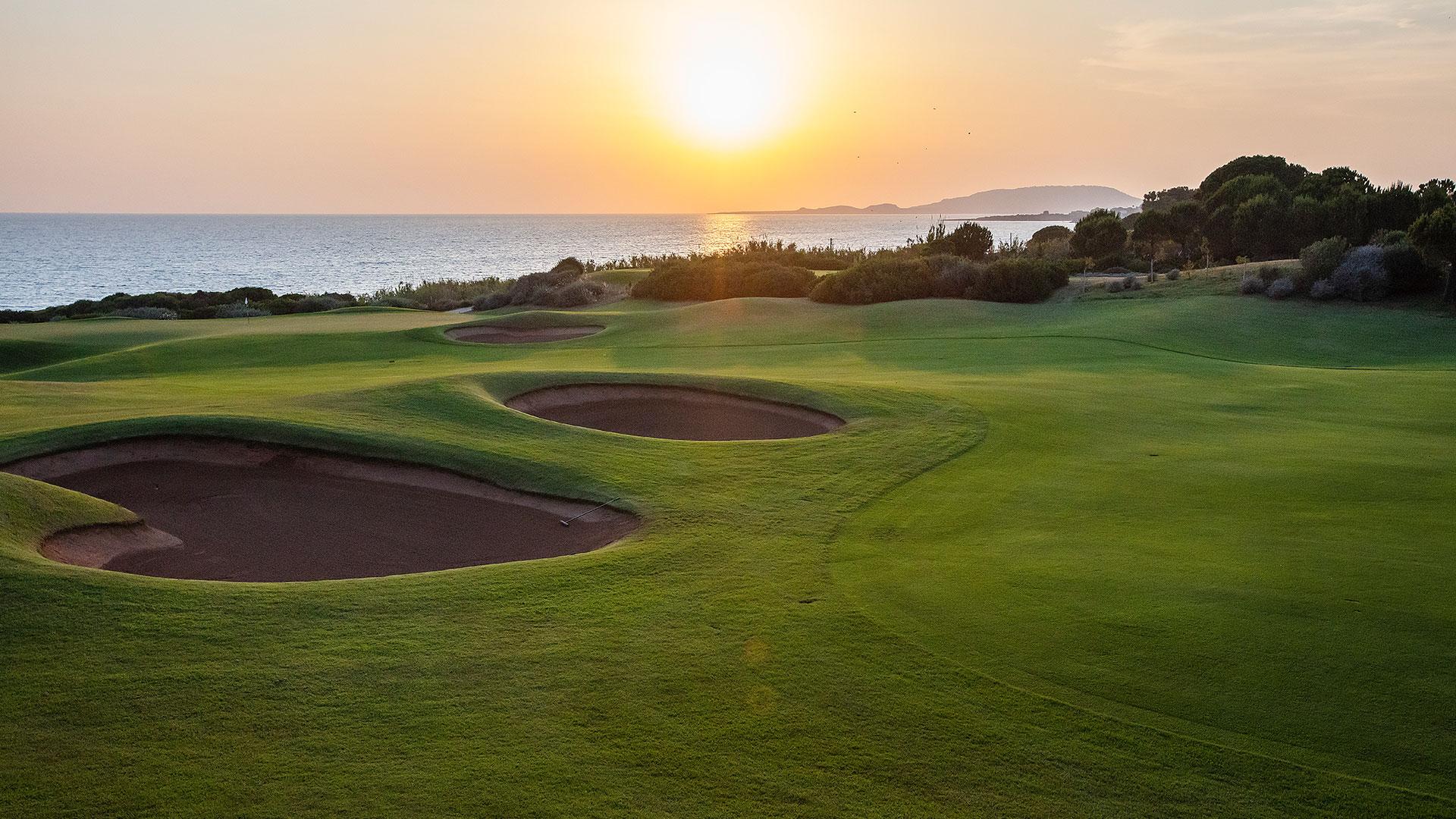 Rolling greens and sand bunkers meet the ocean horizon at sunrise.