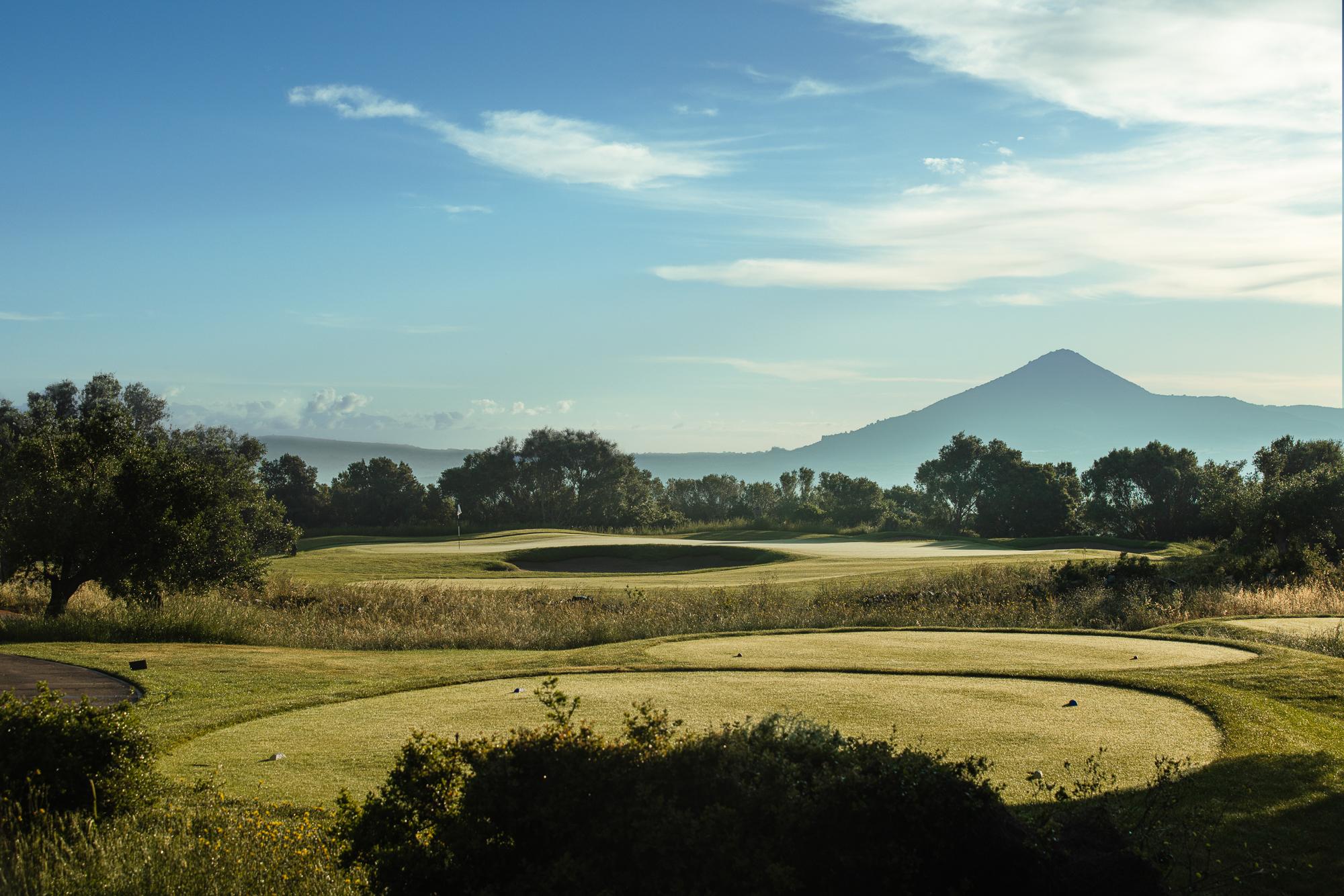 A peaceful green framed by trees with a mountain peak in the distance.