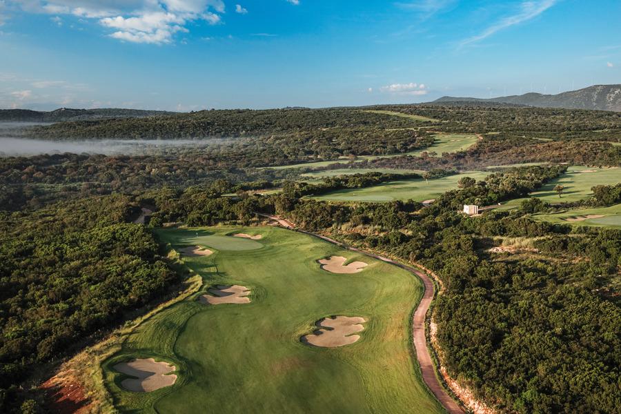 A lush golf course winds through rolling hills with mist hovering above the landscape.