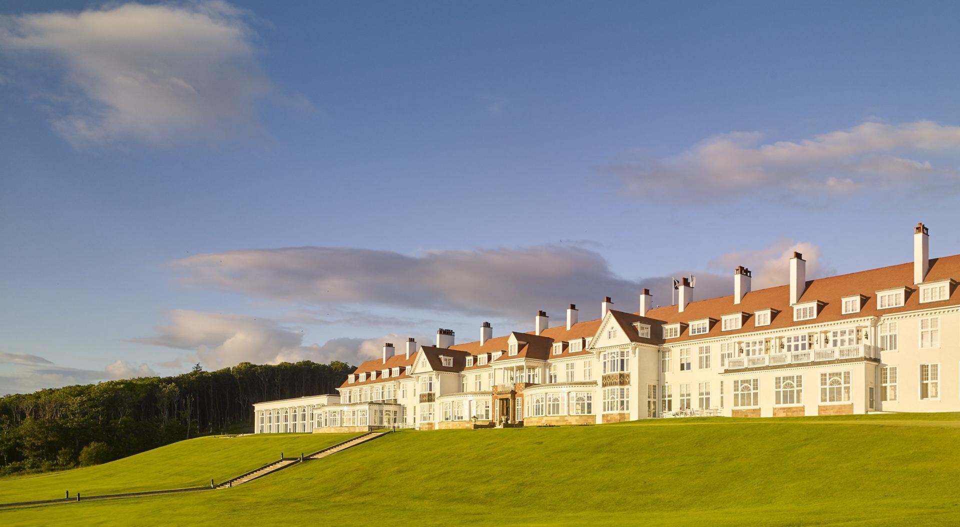 A majestic view of the Trump Turnberry hotel against a backdrop of rolling green hills.