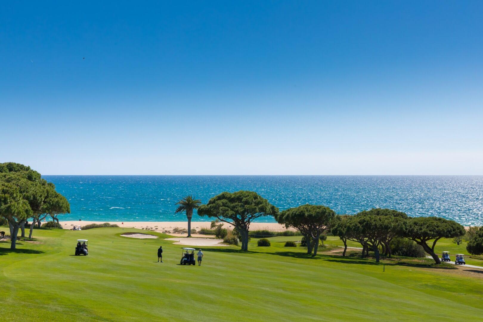Four players using buggies playing their approach shots with the beach in the background