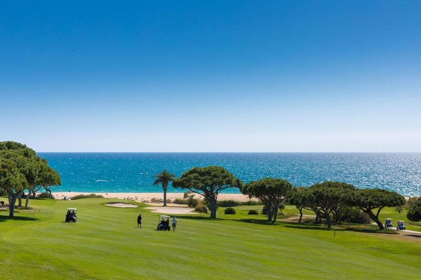 Four players using buggies playing their approach shots with the beach in the background