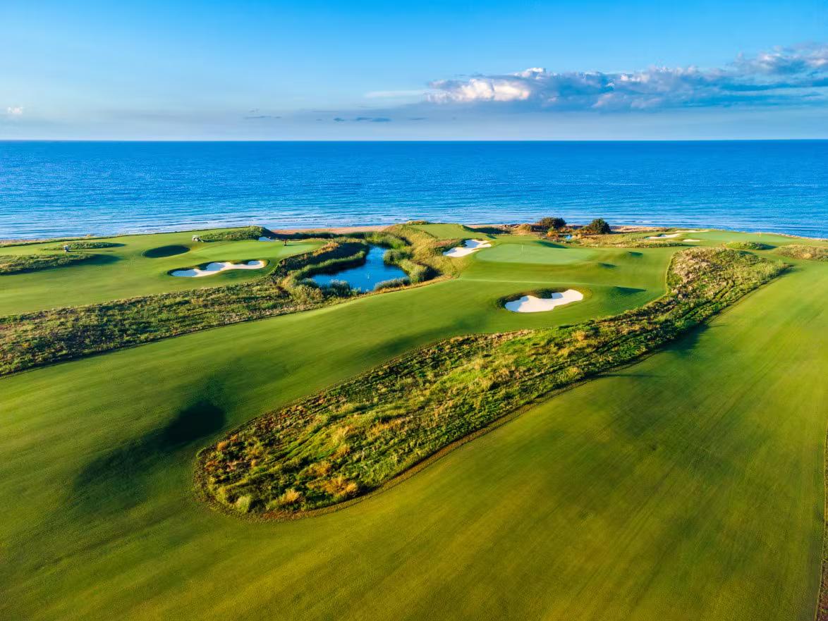 A wide fairway nestled with sand bunkers leading to a smooth green with sea views
