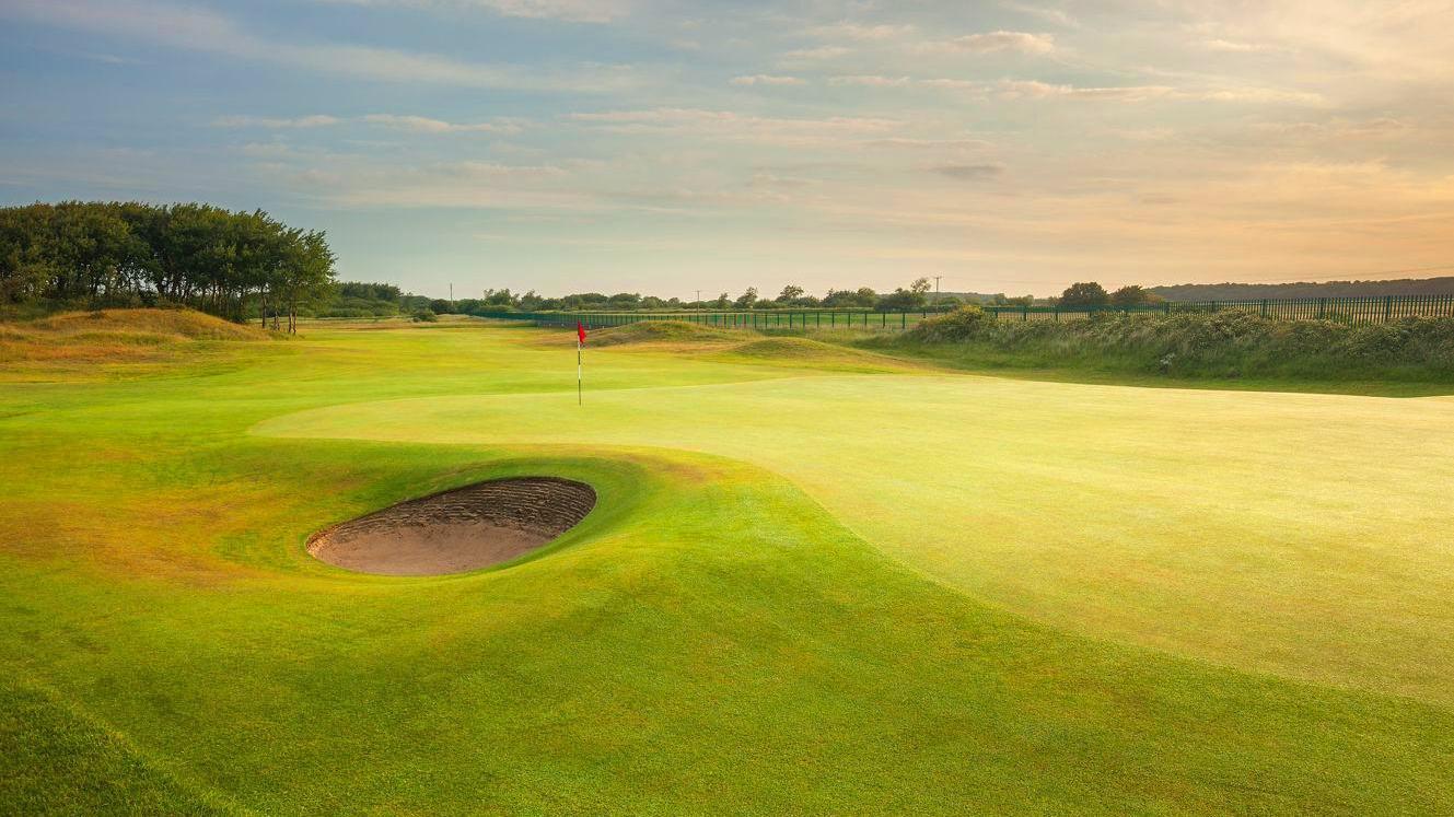 A golden-lit green with a single bunker near the edge.