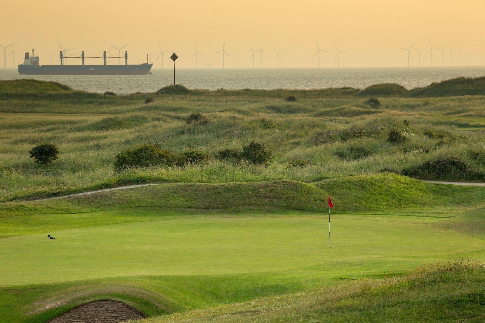 A serene view of the course with a ship and wind turbines in the distance