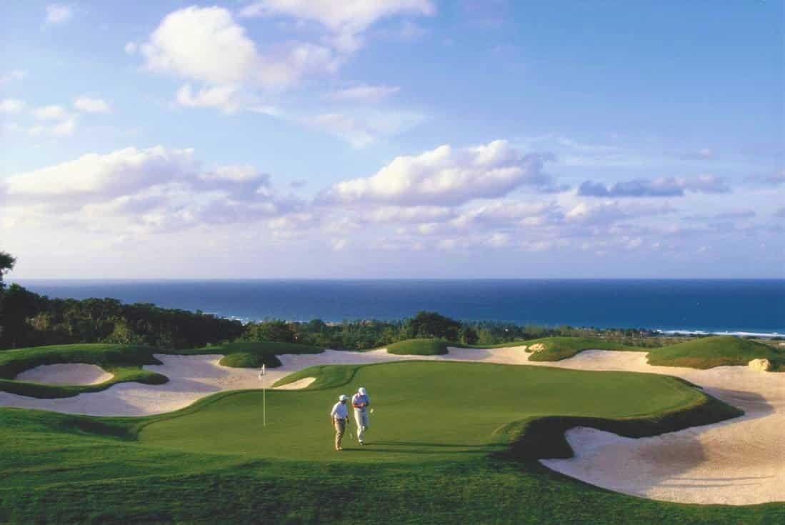 Golfers play on a pristine green surrounded by perfectly sculpted bunkers and ocean views.