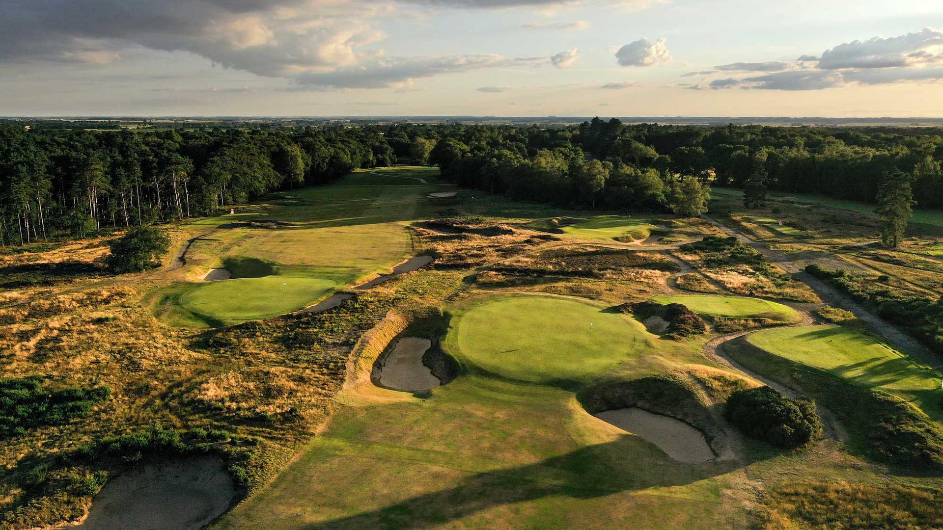Aerial view of multiple greens and fairways among dense trees.