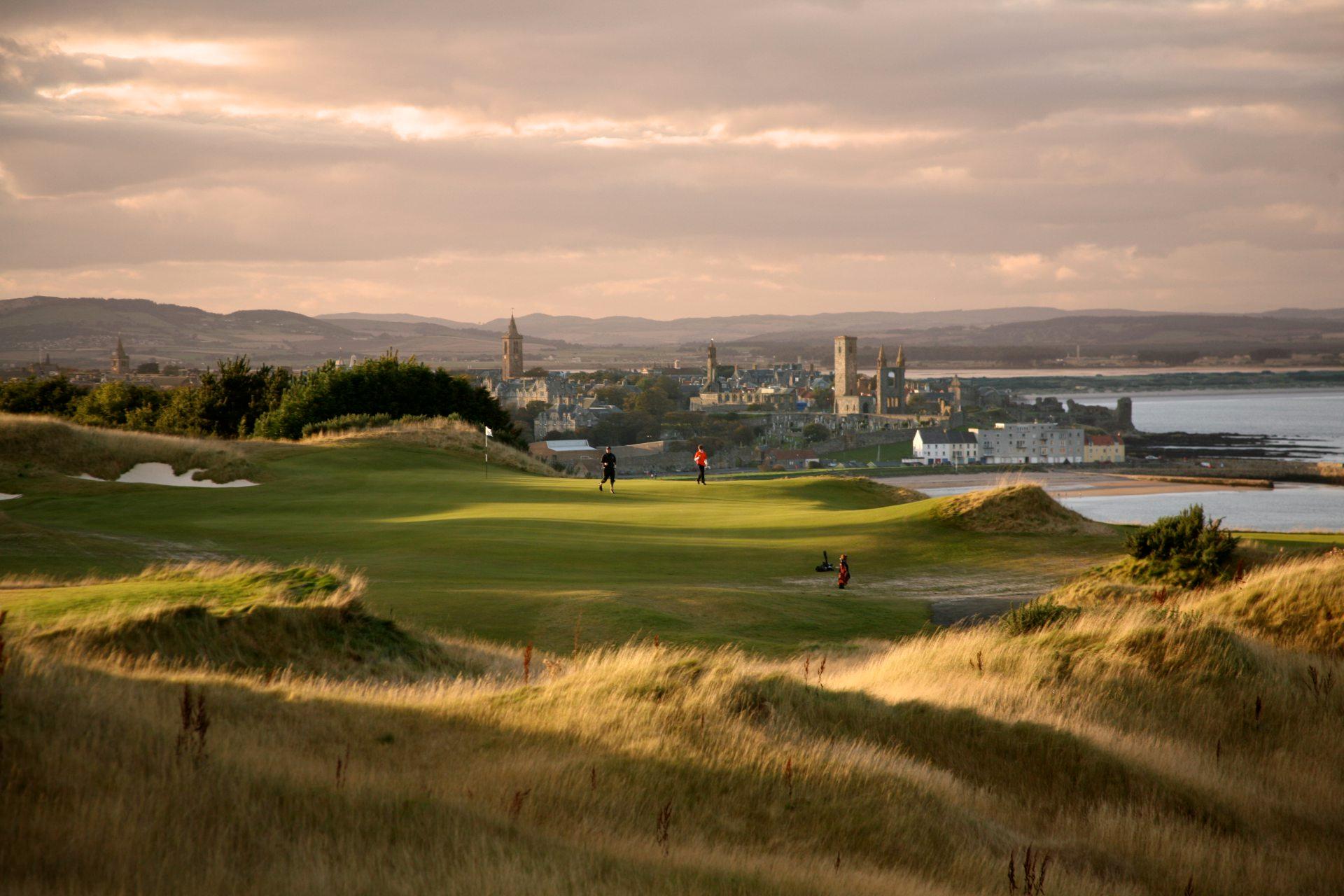 Three players around a green with the town of St Andrews in the background