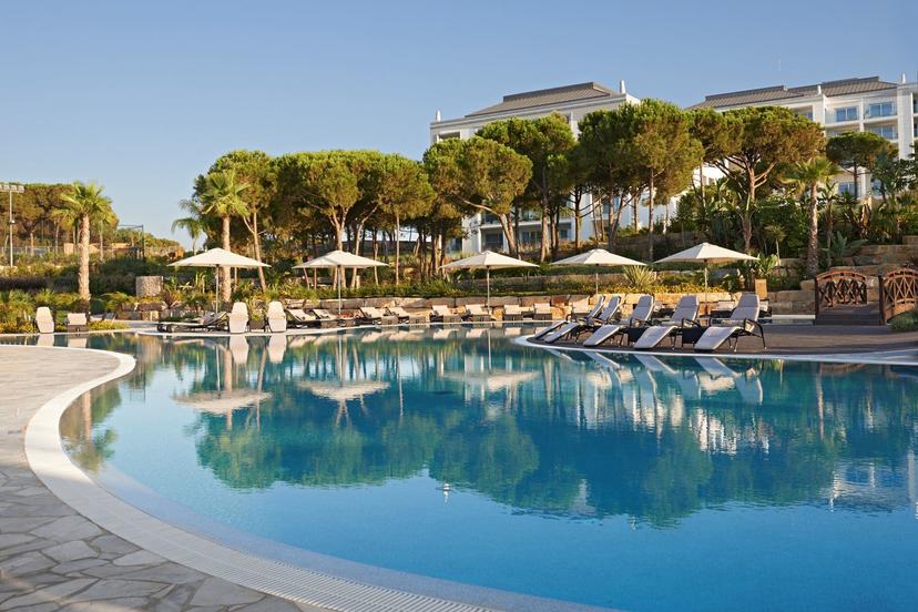 A serene pool reflecting the surrounding trees and umbrellas under clear blue skies