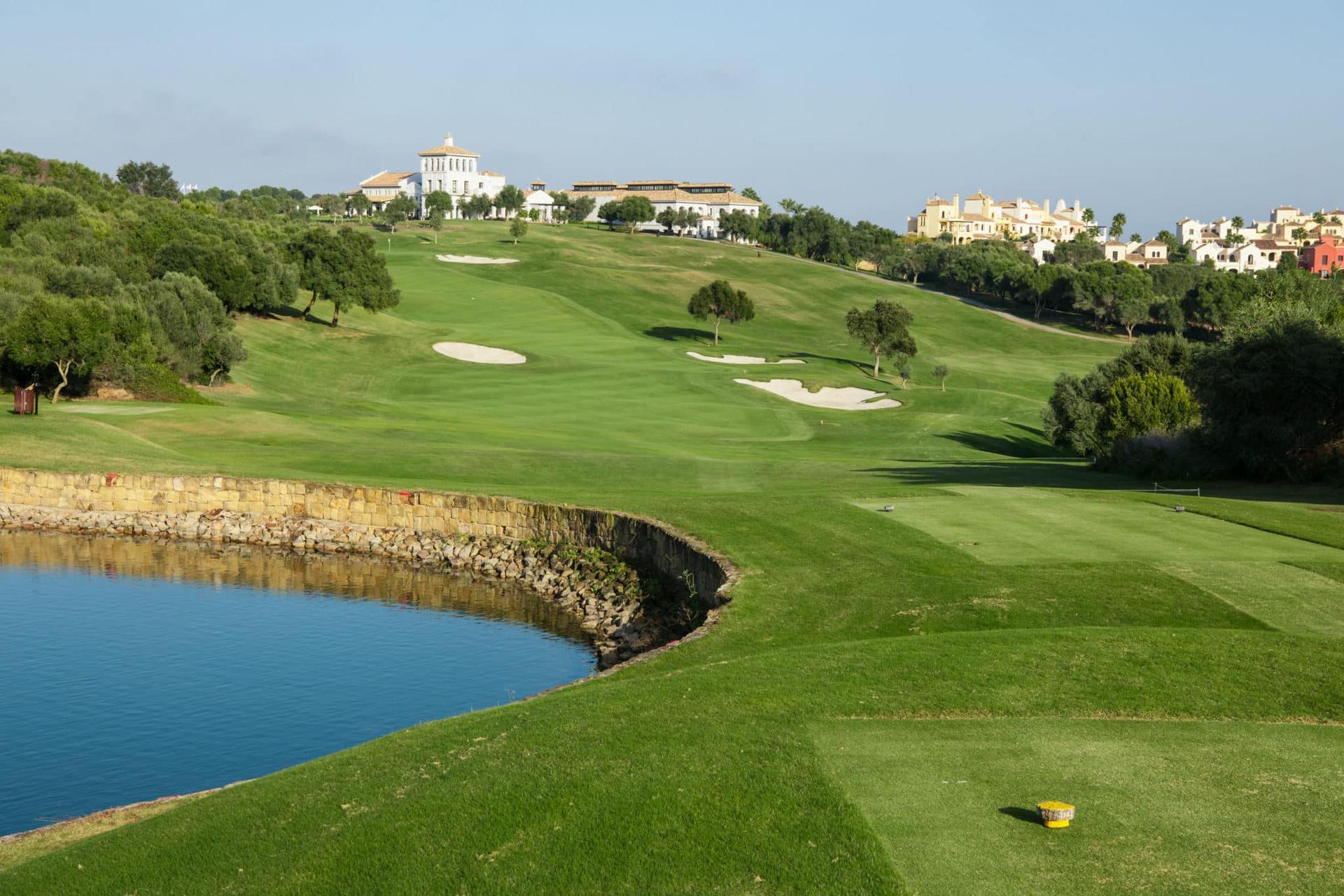 A uphill fairway leading to a smooth green surrounded by sand bunkers with the clubhouse at the top of the hill