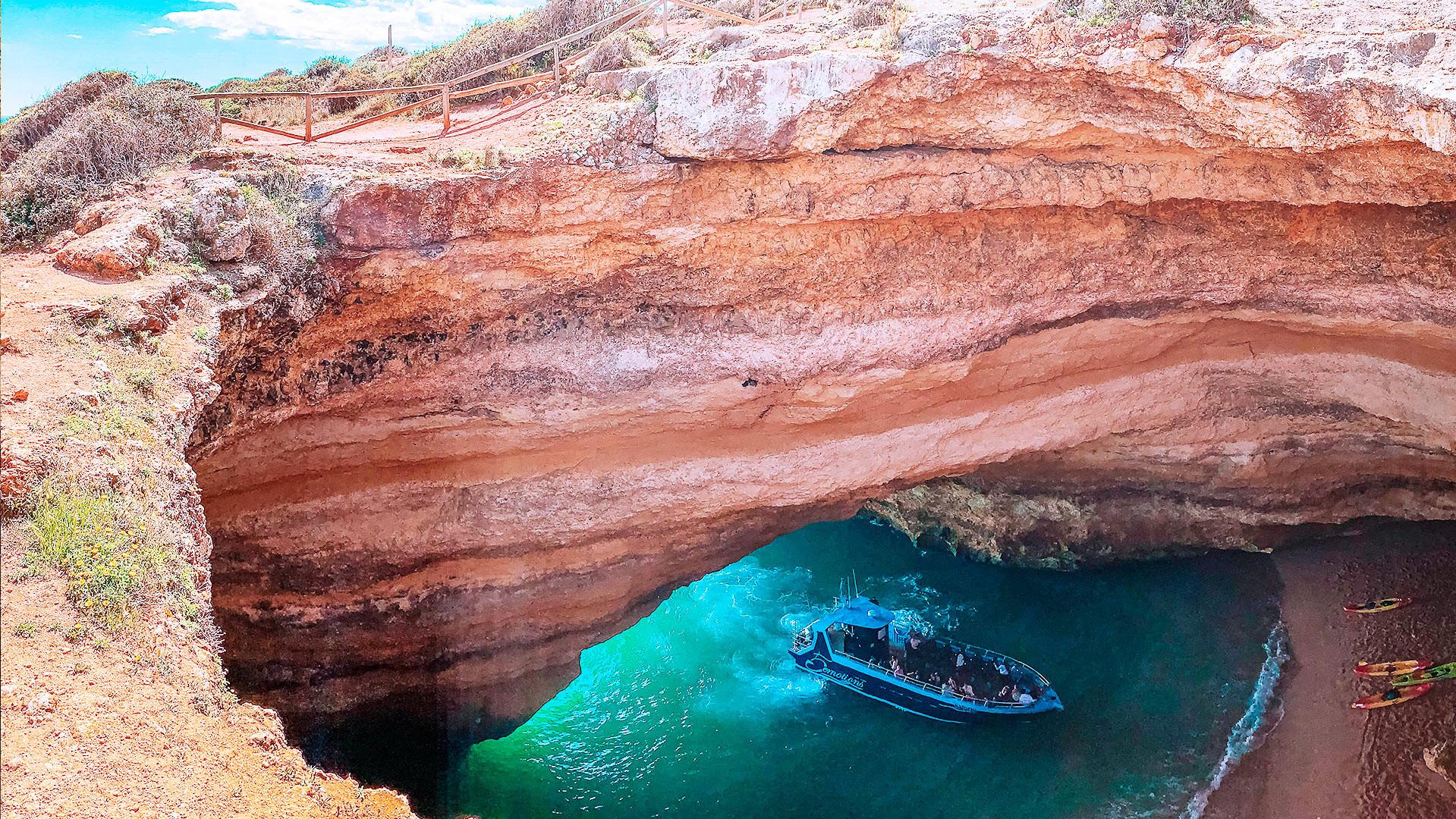 A overhead view of a cave with paddle boards on the beach and a tour boat pulling in