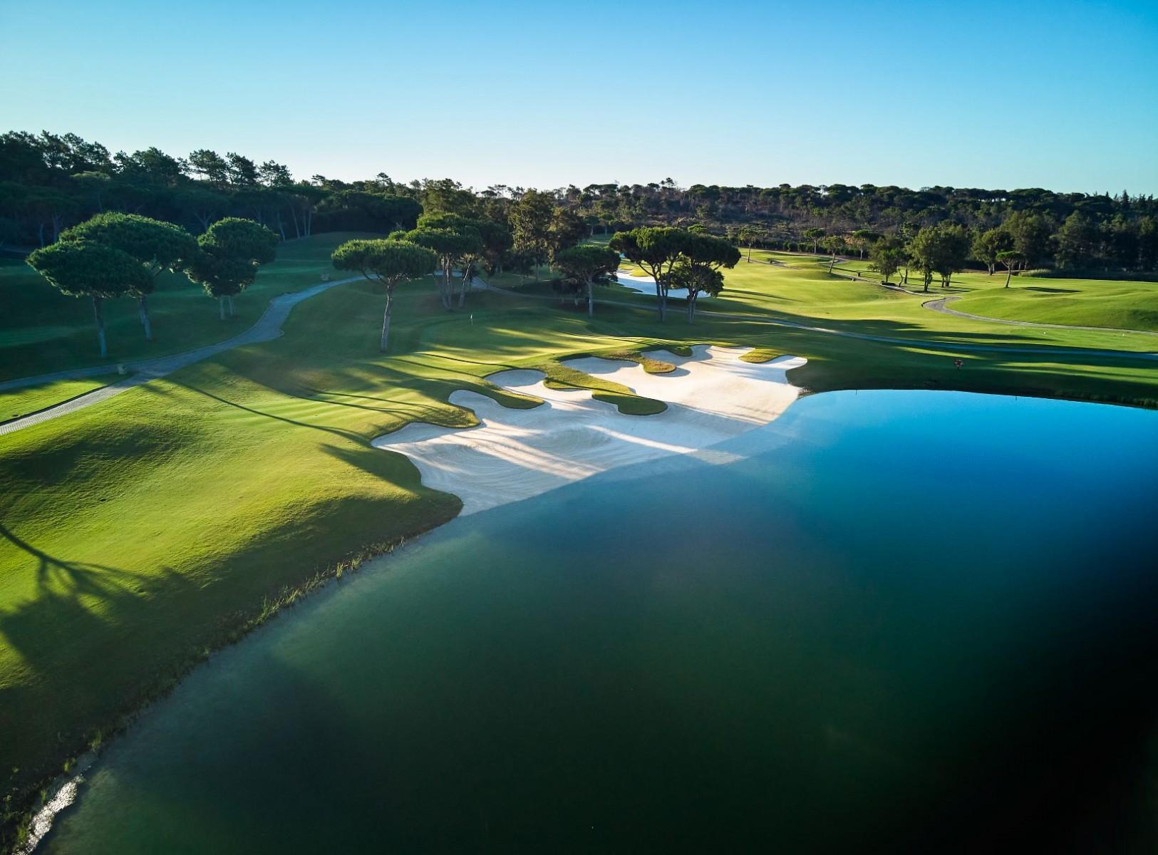 Overhead view of a large sand bunker sandwiched between a manicured green and a water hazard