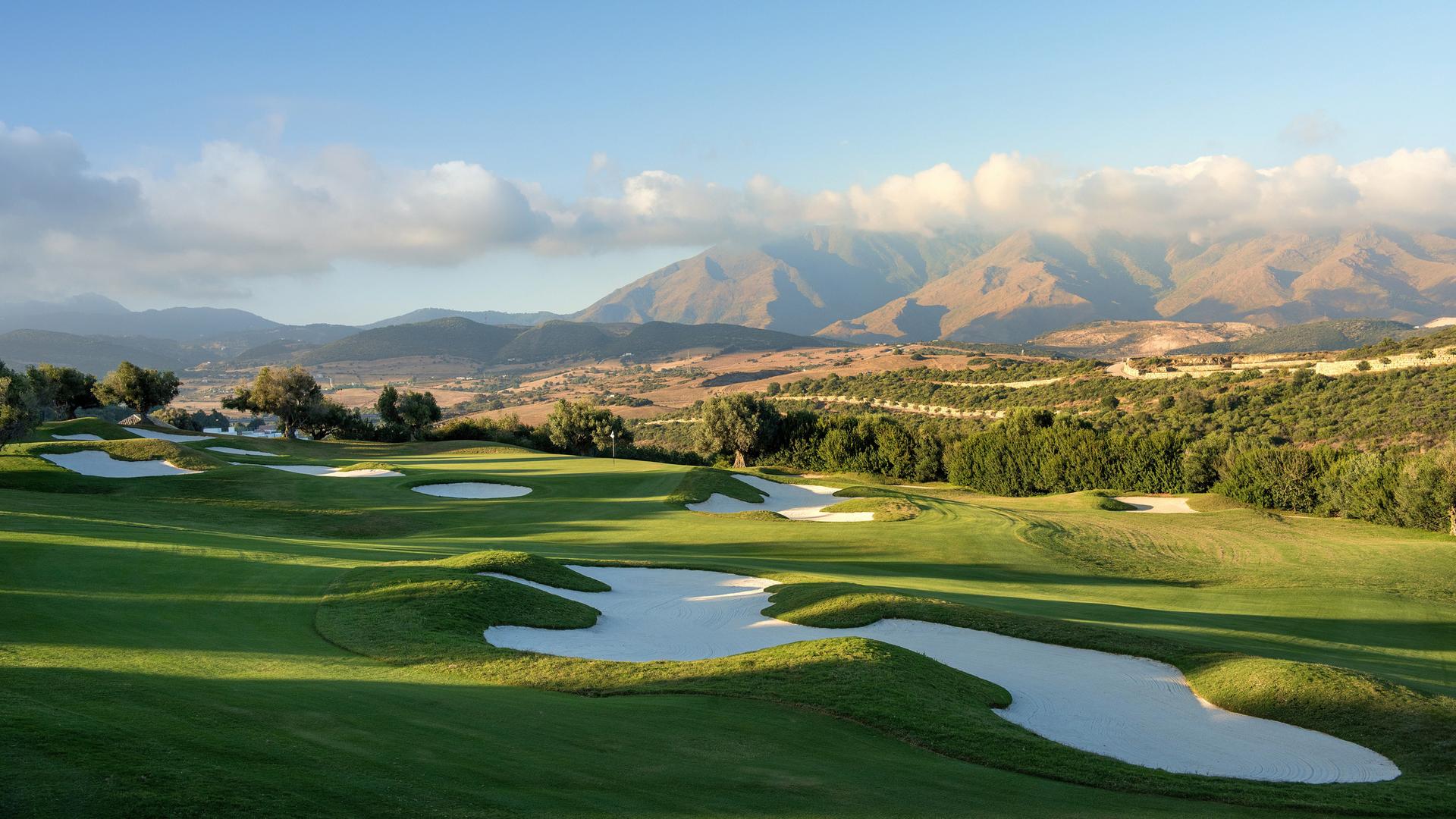A smooth green surrounded by sand bunkers with distant mountain views