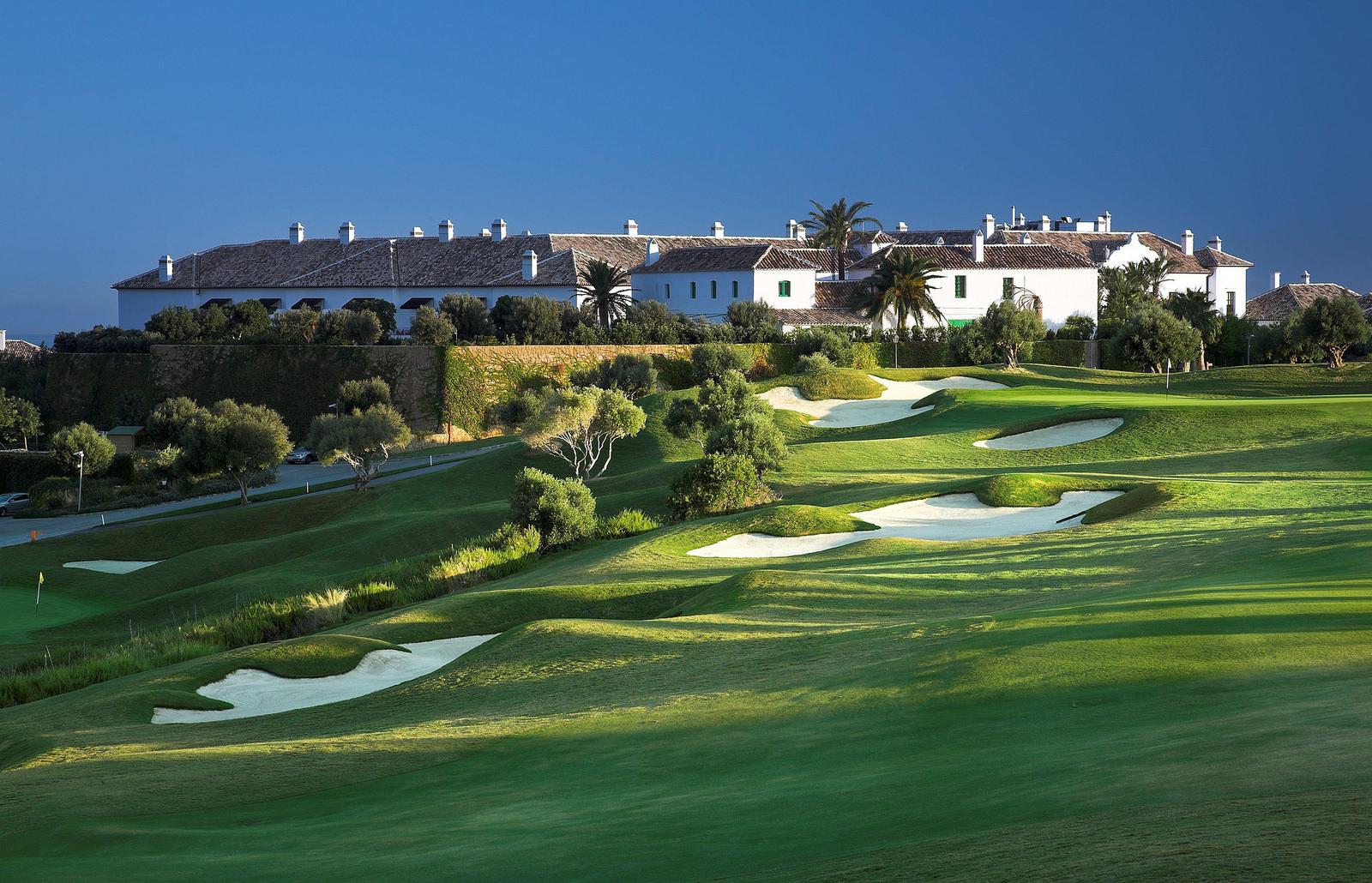 The clubhouse overlooking a downhill fairway littered with sand bunkers under blue skies