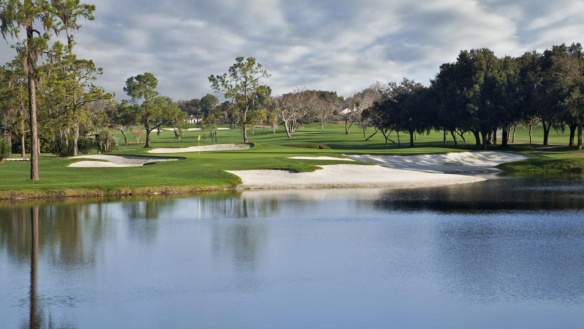 A smooth green surrounded by large sand bunkers strategically placed next to a water hazard