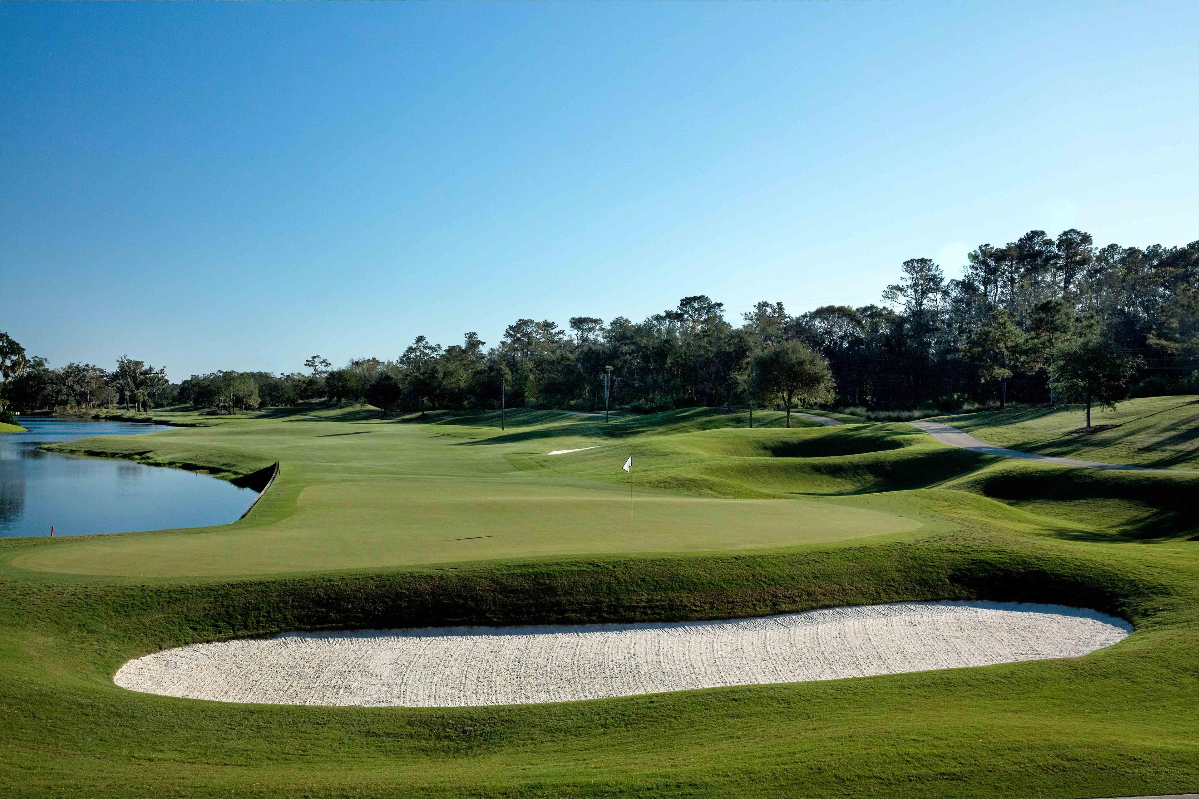 A wide fairway running along a water hazard leading to a smooth green surrounded by sand bunkers