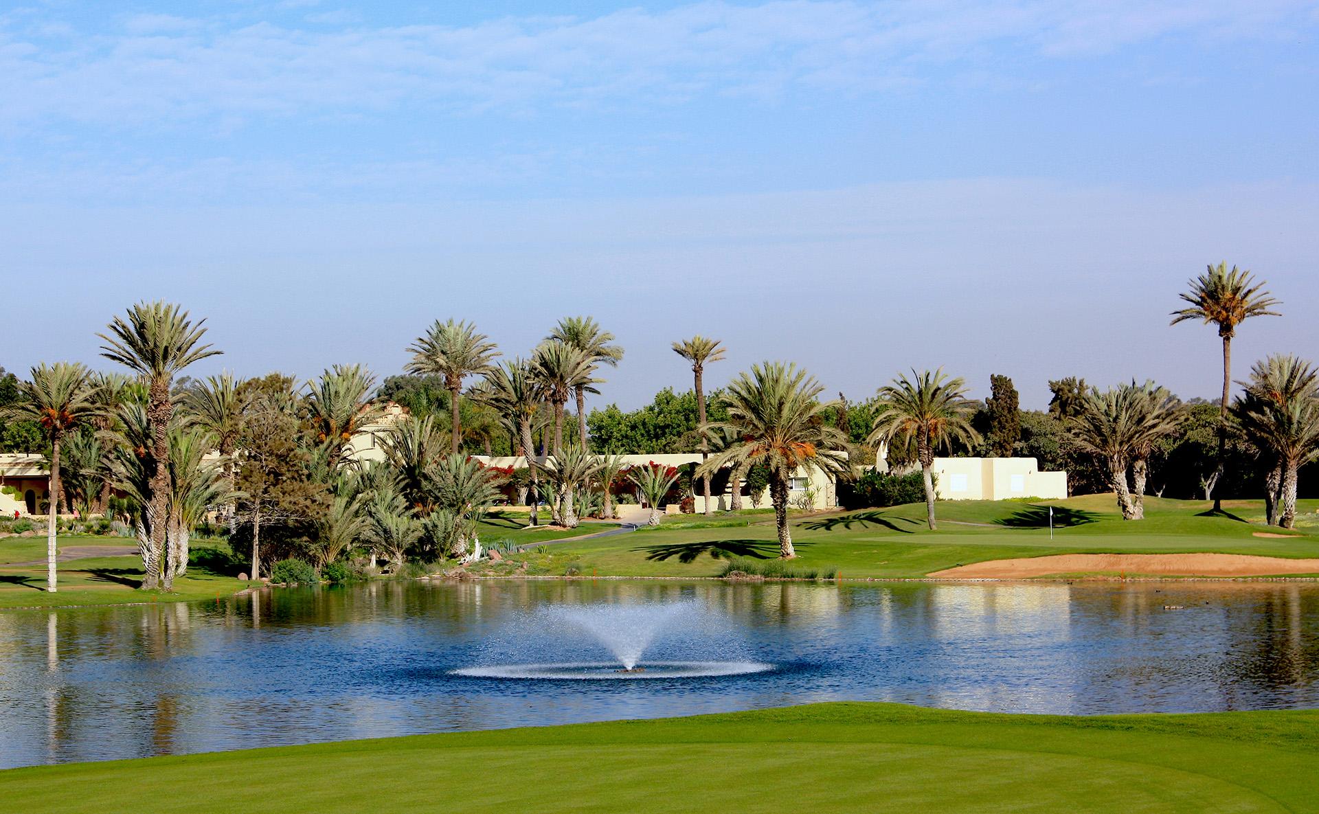 A water fountain in the centre of a water hazard with palm trees on the course
