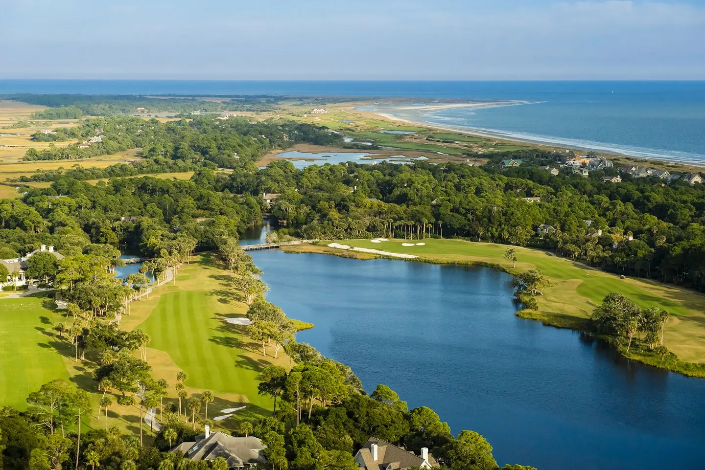 Aerial view of the course with a large water hazard through the middle and the Atlantic Ocean in the background