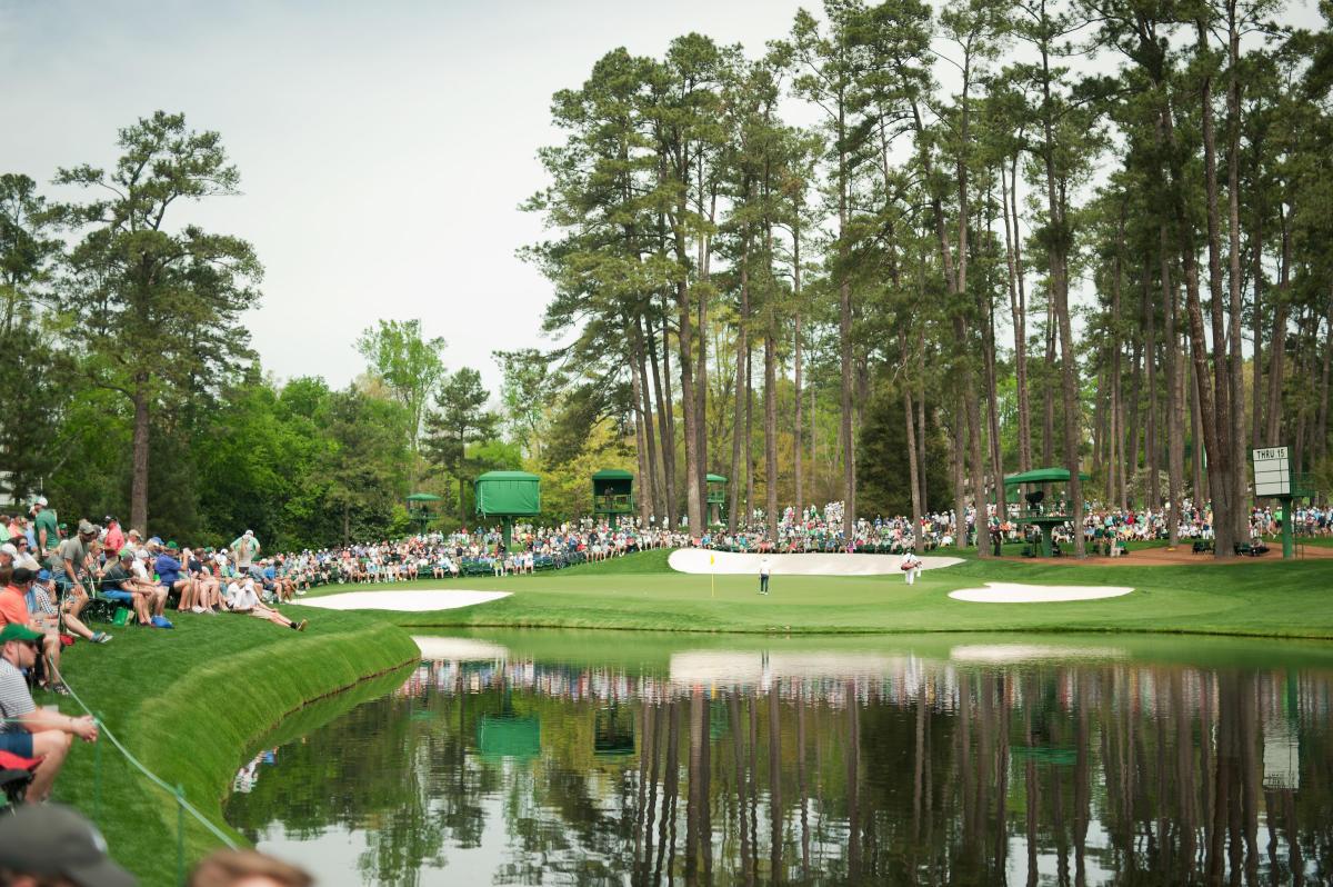 View over water hazard to the green surrounded by crowds