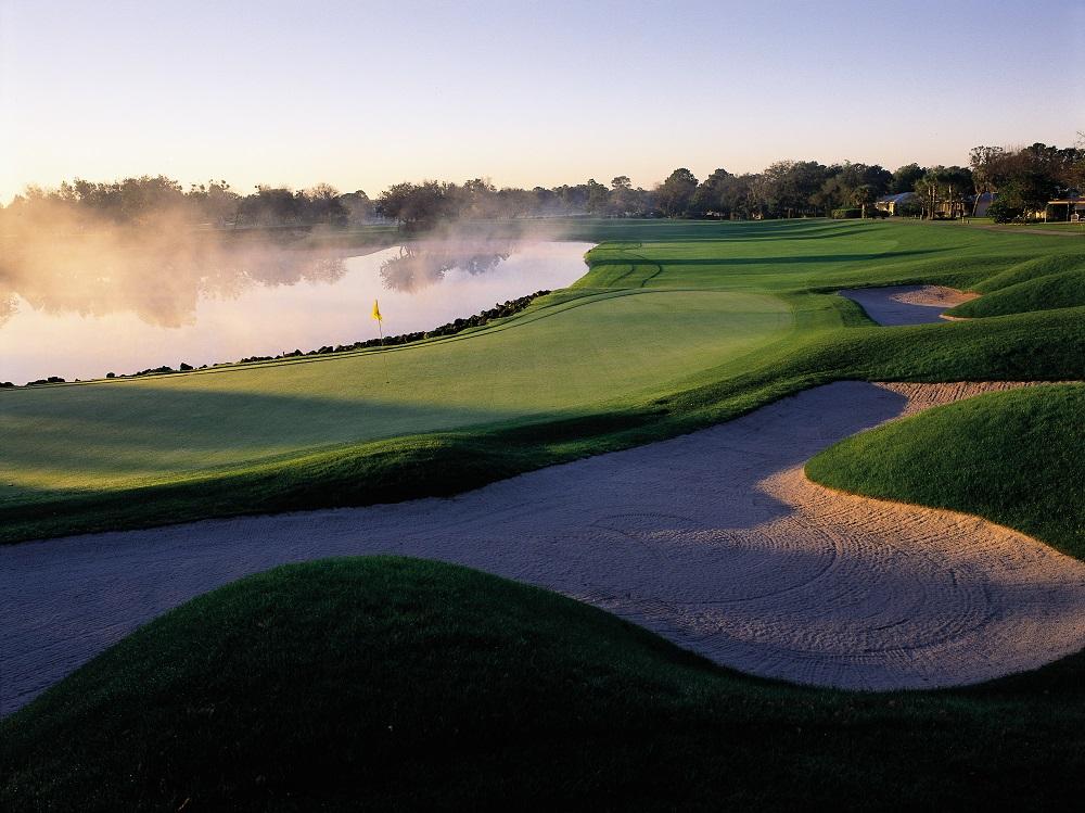 View of the 18th green with mist rising from the water hazard behind and bunkers in the foreground
