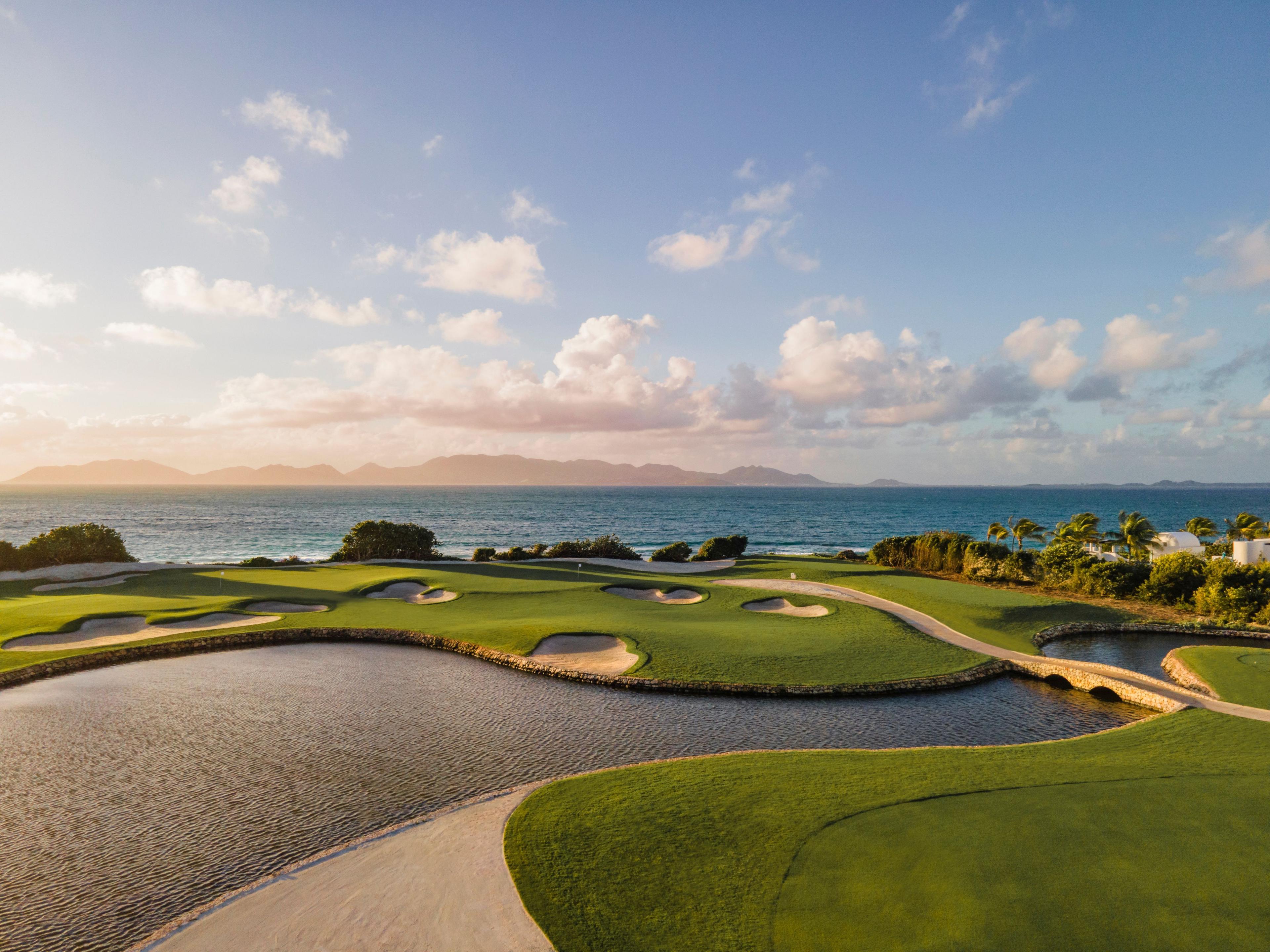 Panoramic view of a smooth green separated by a water hazard with a bridge to navigate the course