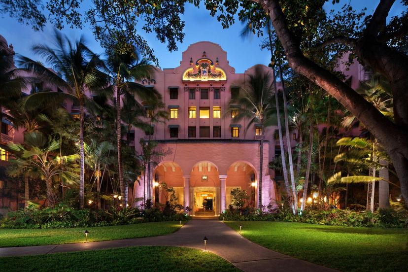 Exterior view of the hotel building being lit up at evening surrounded by jungle trees