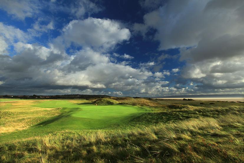 Panoramic view of a winding fairway leading to a smooth green under cloudy skies