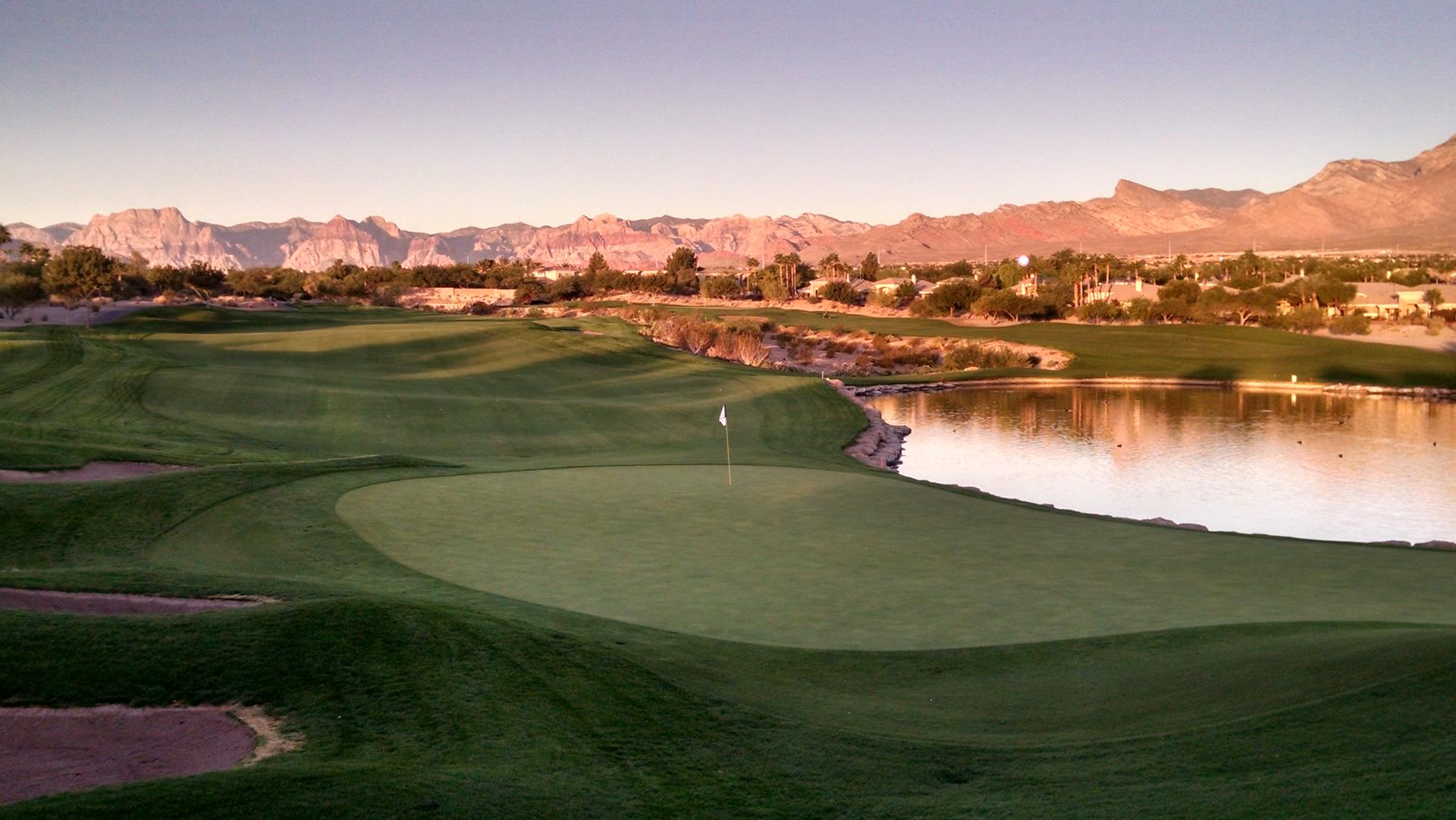 Panoramic view of a manicured green next to a water hazard with the sun reflecting off it