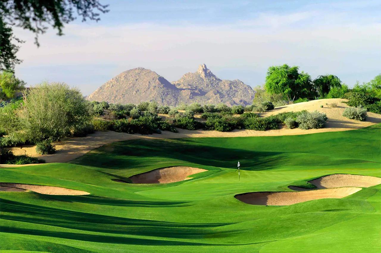 A manicured green surrounded by a deep sand bunker with mountains views in the distance