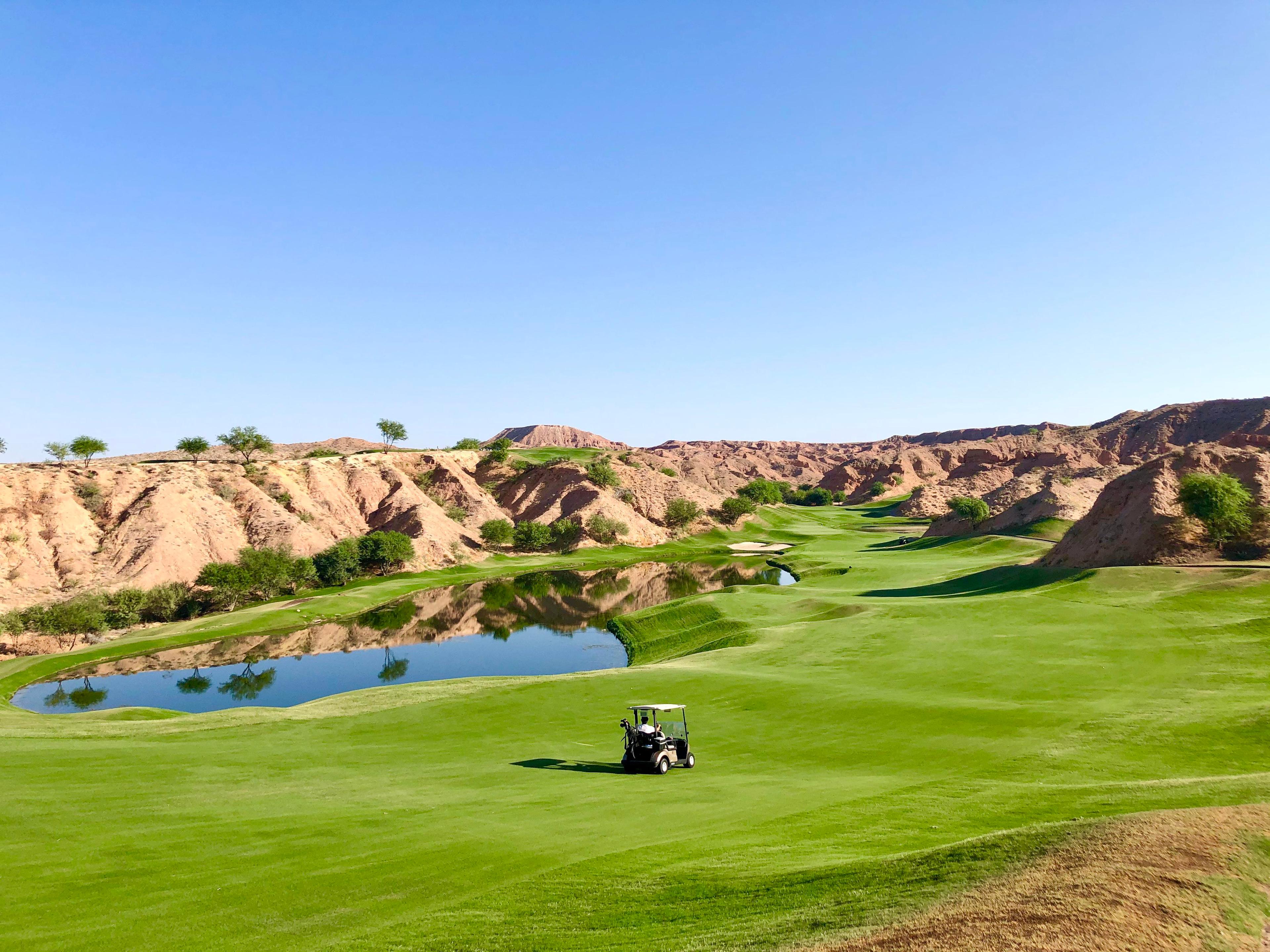 Panoramic view of a buggy driving down a fairway surrounded by a mountainous landscape