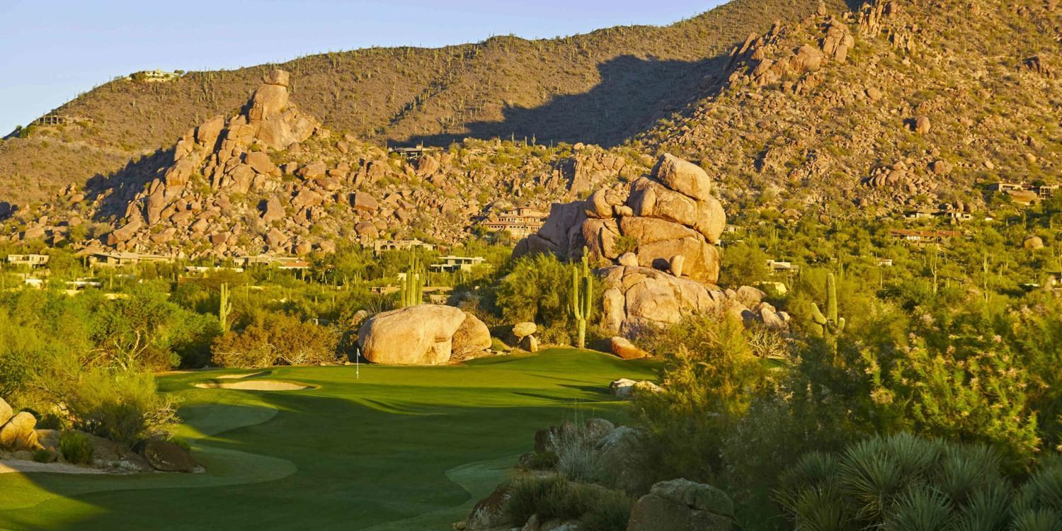 Manicured green with a strategically placed sand bunker and mountains in the back